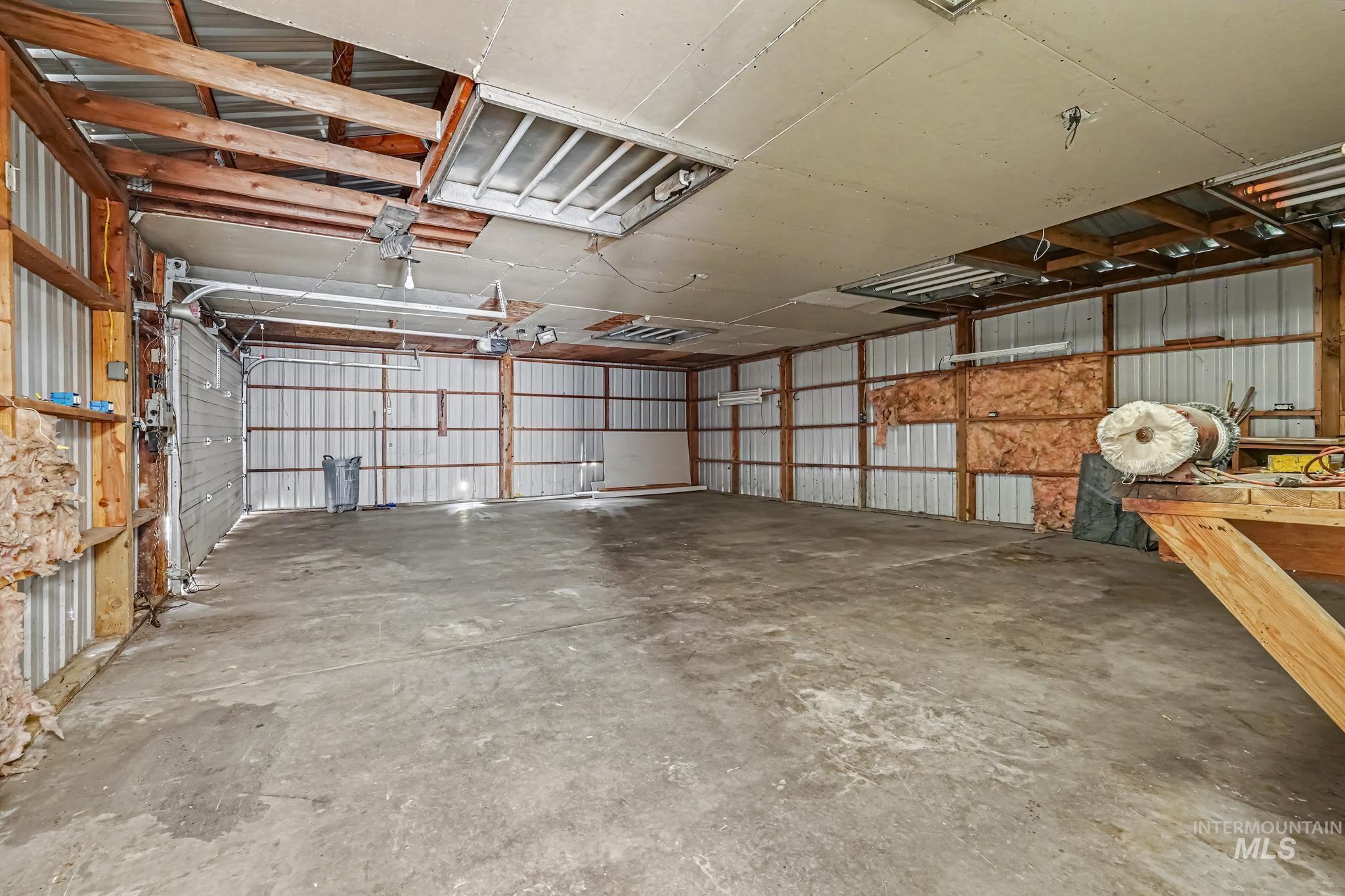 Spacious workshop featuring a concrete floor, corrugated metal walls, exposed wood framing, and multiple overhead light fixtures