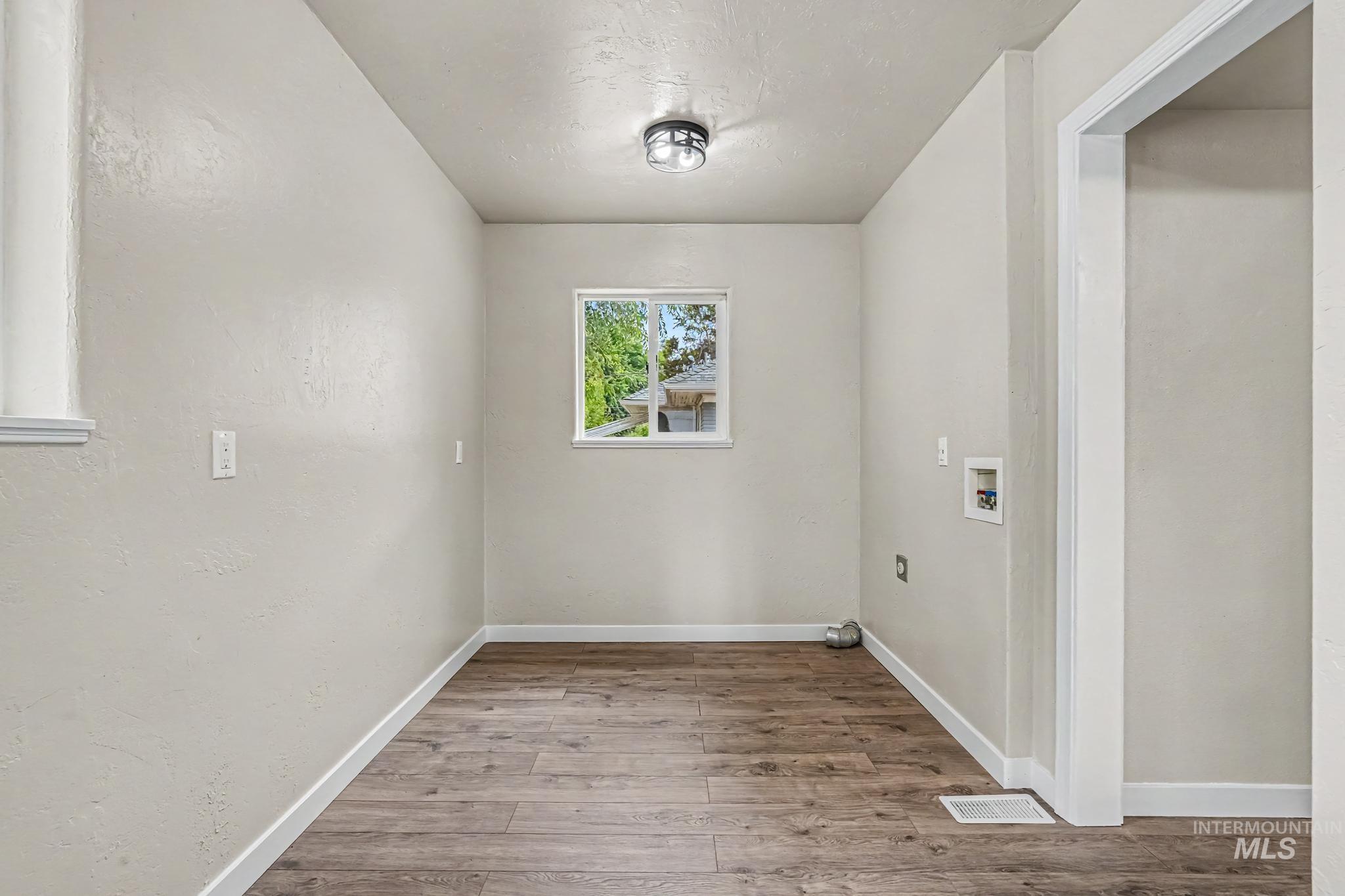 Dedicated utility space featuring wood-finish flooring, light neutral wall tones, and a window for natural illumination