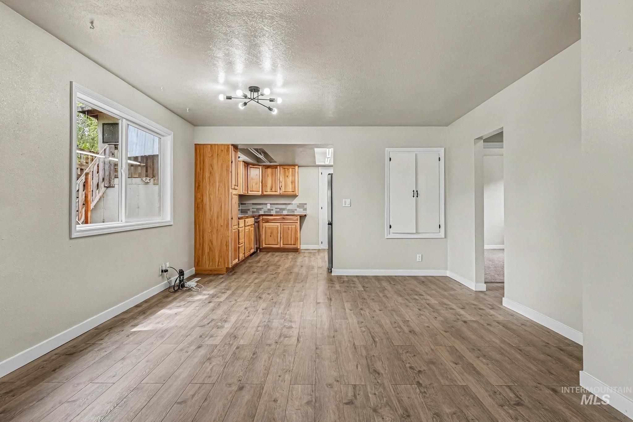 Open concept living space featuring wood-finish flooring, a modern sputnik-style light fixture, and a kitchen with wood cabinetry and a tiled backsplash