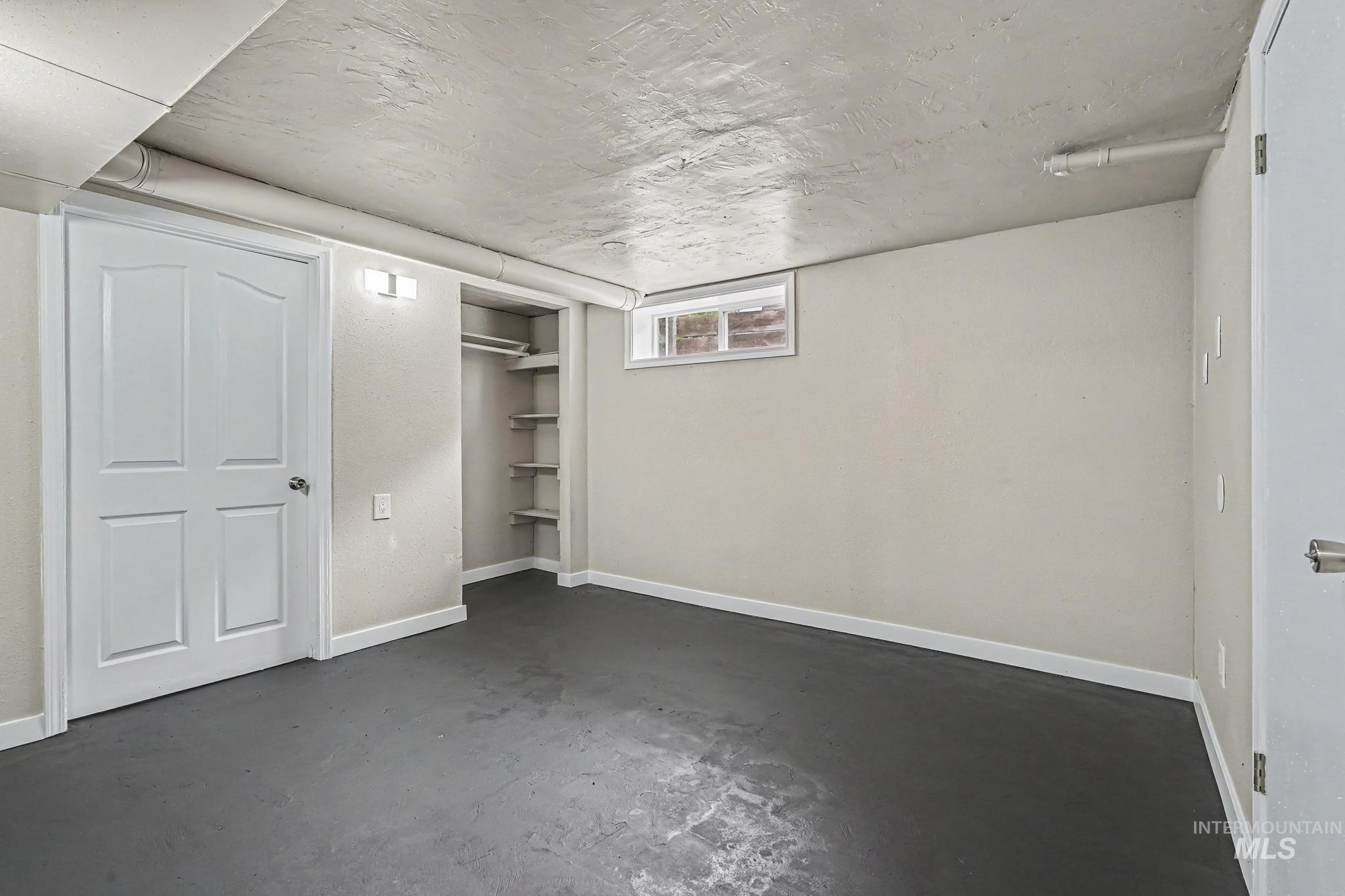 Finished room featuring painted concrete flooring, an egress window, and a built-in closet with shelving and hanging rod