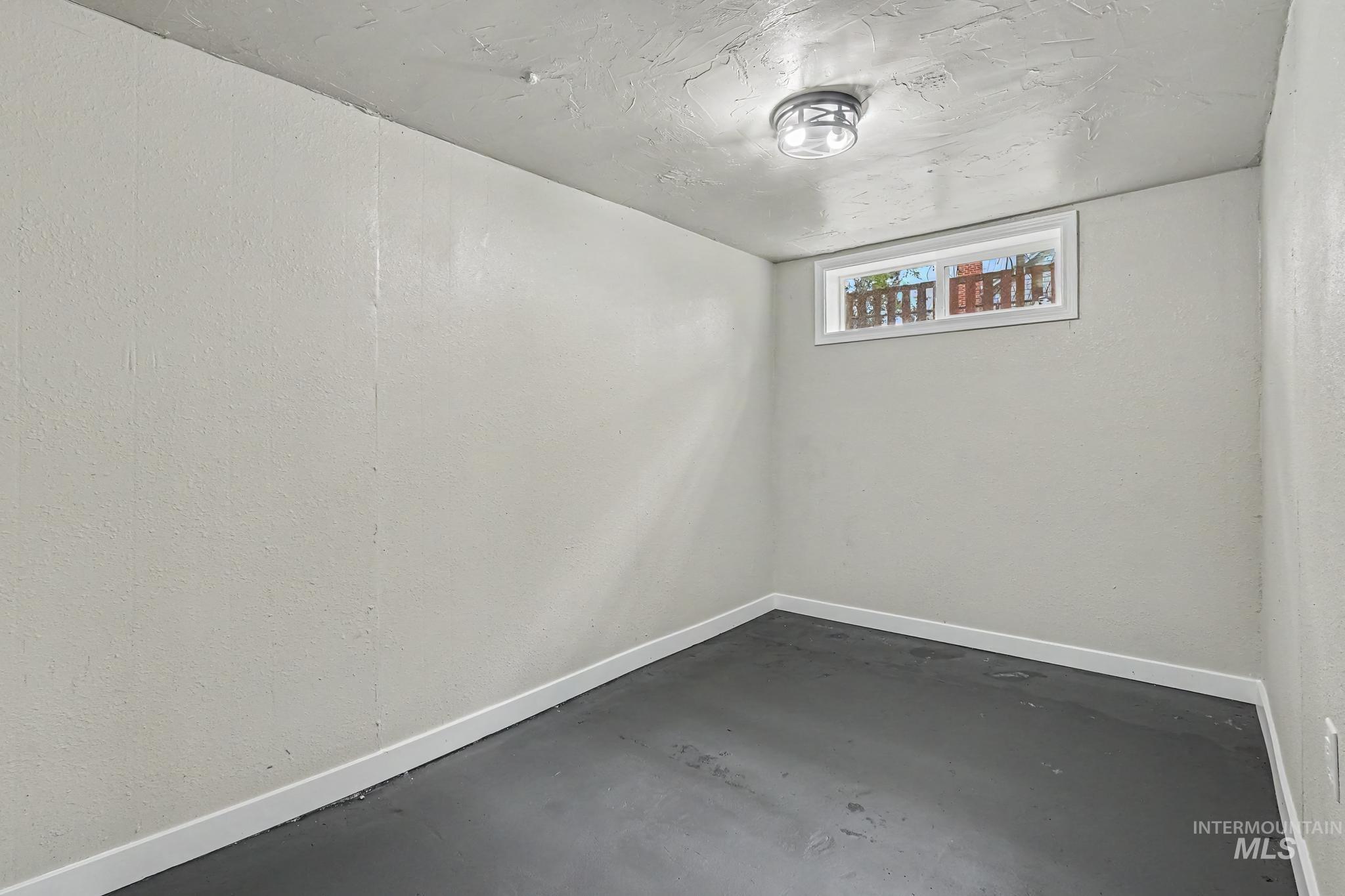 Room featuring light-colored walls, dark flooring, white baseboards, and a single ceiling light fixture