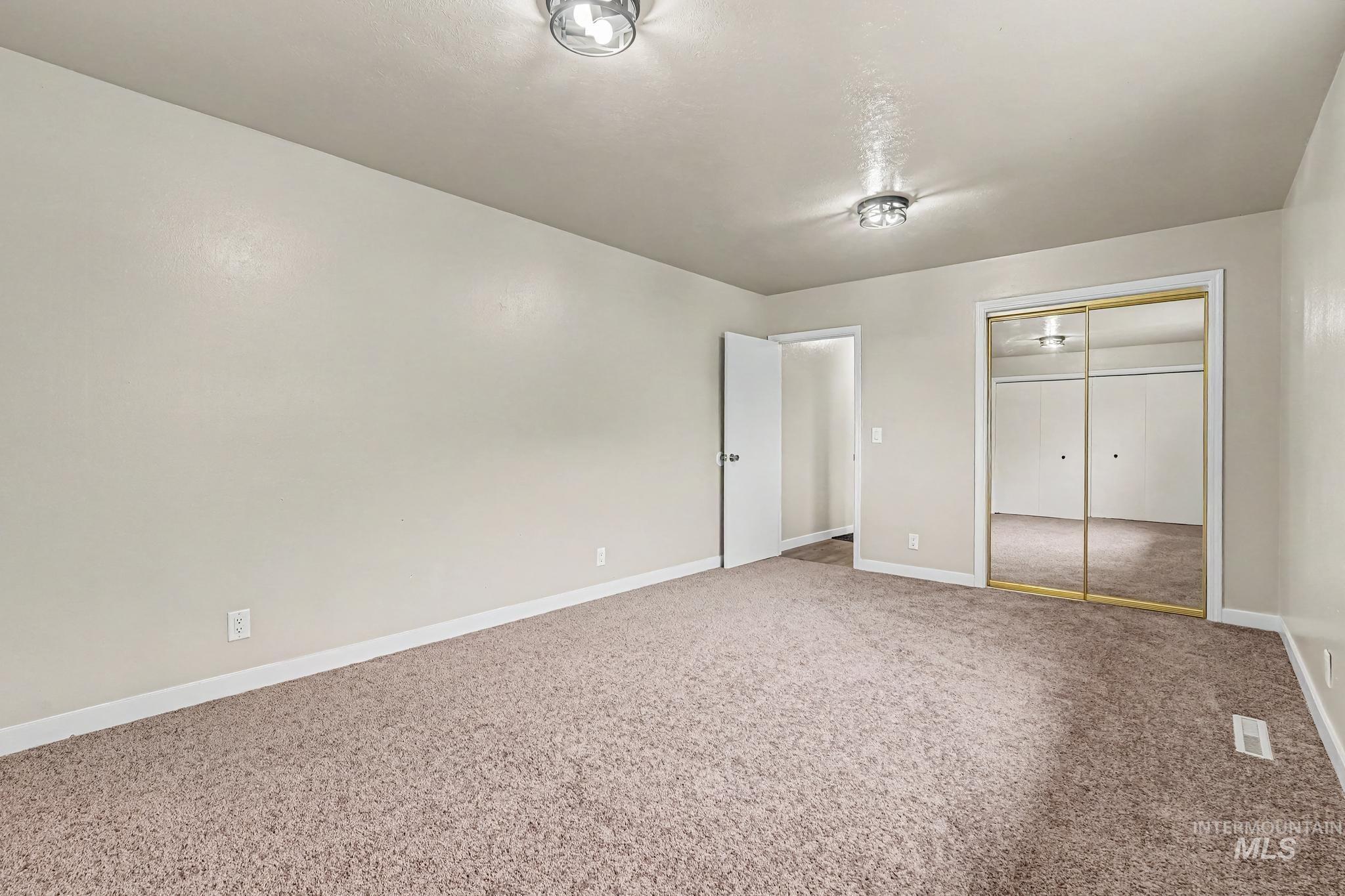 Spacious room featuring neutral carpeting, light-toned walls, and white baseboards