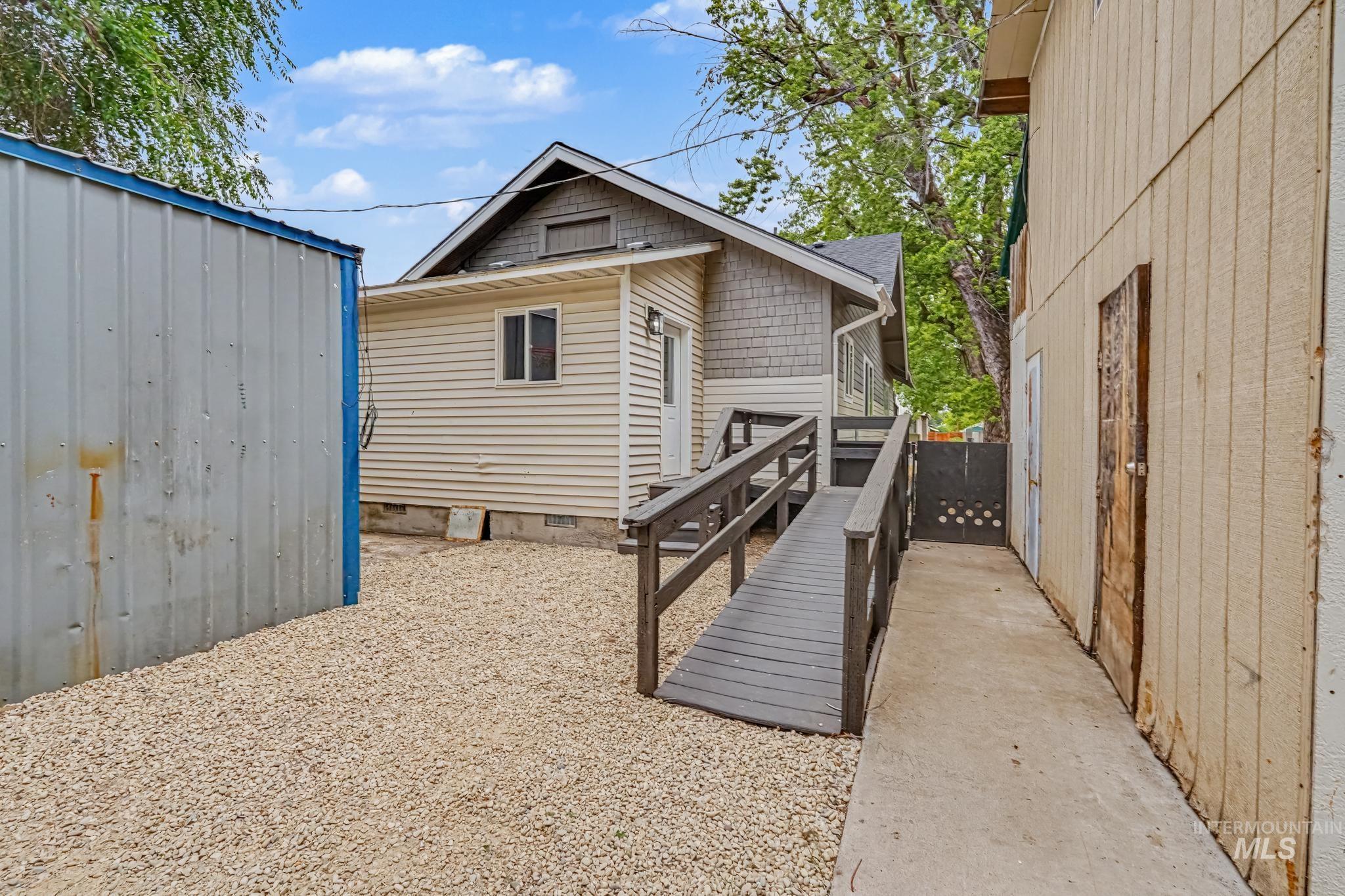 Exterior property featuring a wooden ramp leading to a rear entrance, gravel ground cover, and a concrete pathway