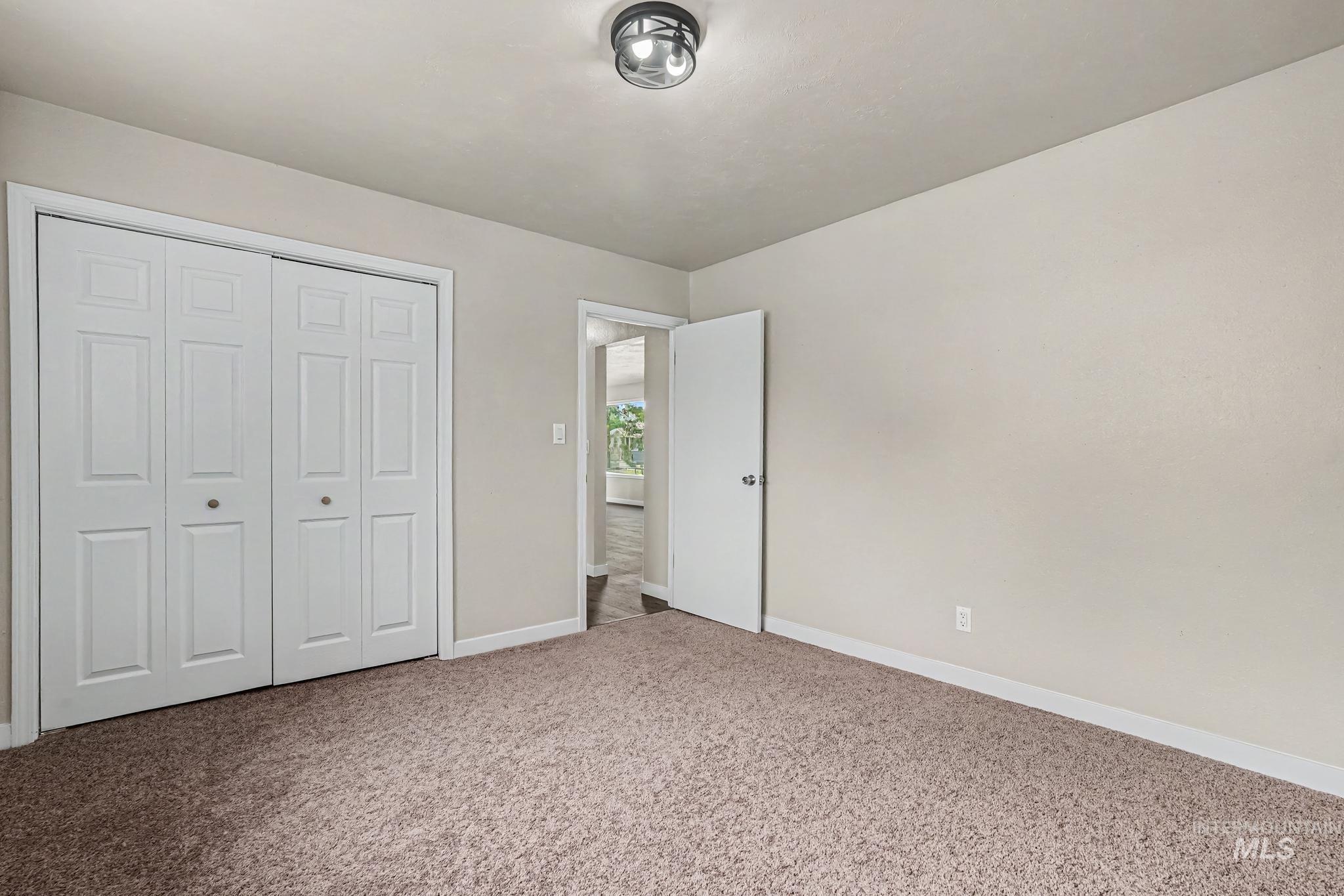 Carpeted room featuring a white bi-fold closet, a white interior door, a flush-mount ceiling light fixture, and light-colored walls