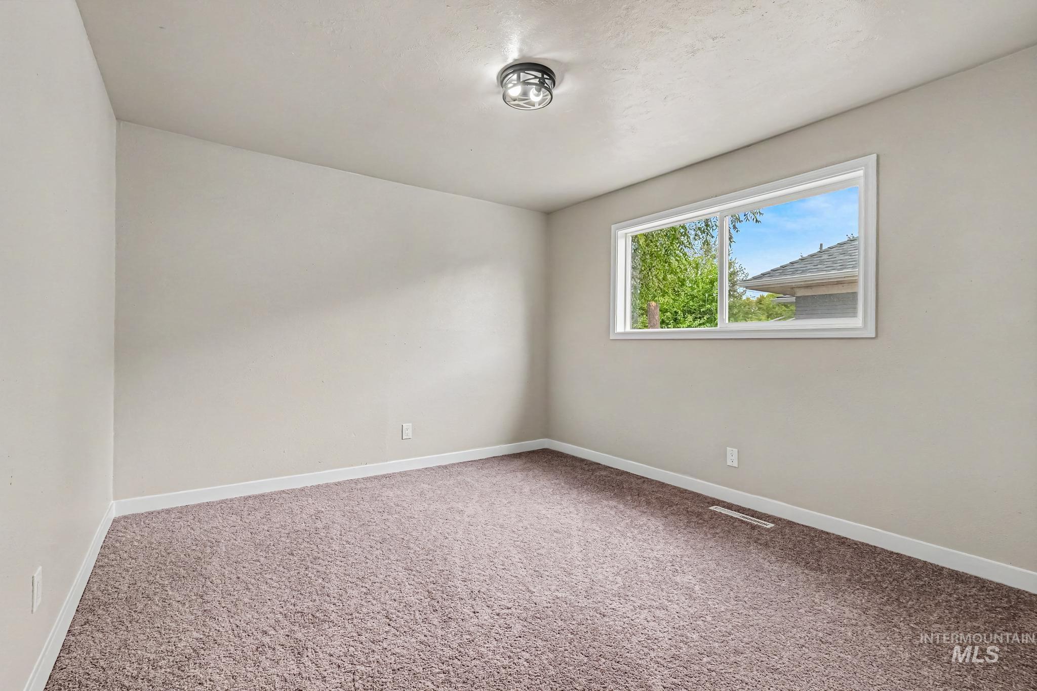 Spacious room featuring neutral-toned walls, brown carpeting, and white baseboards