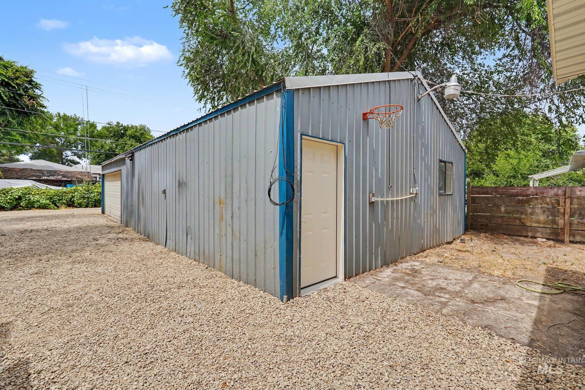 Corrugated metal outbuilding featuring a side entry door, single window, and an attached basketball hoop