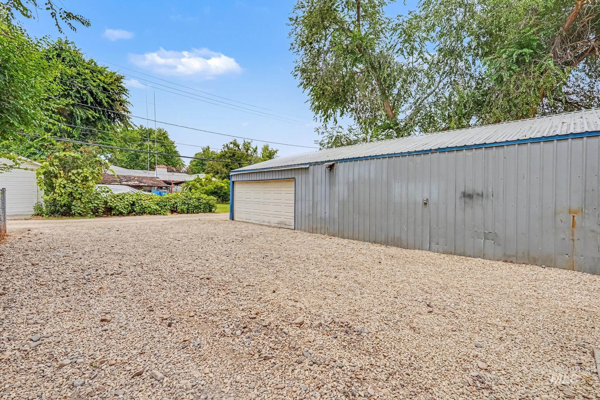 Expansive gravel yard with a large metal-sided outbuilding featuring a roll-up garage door