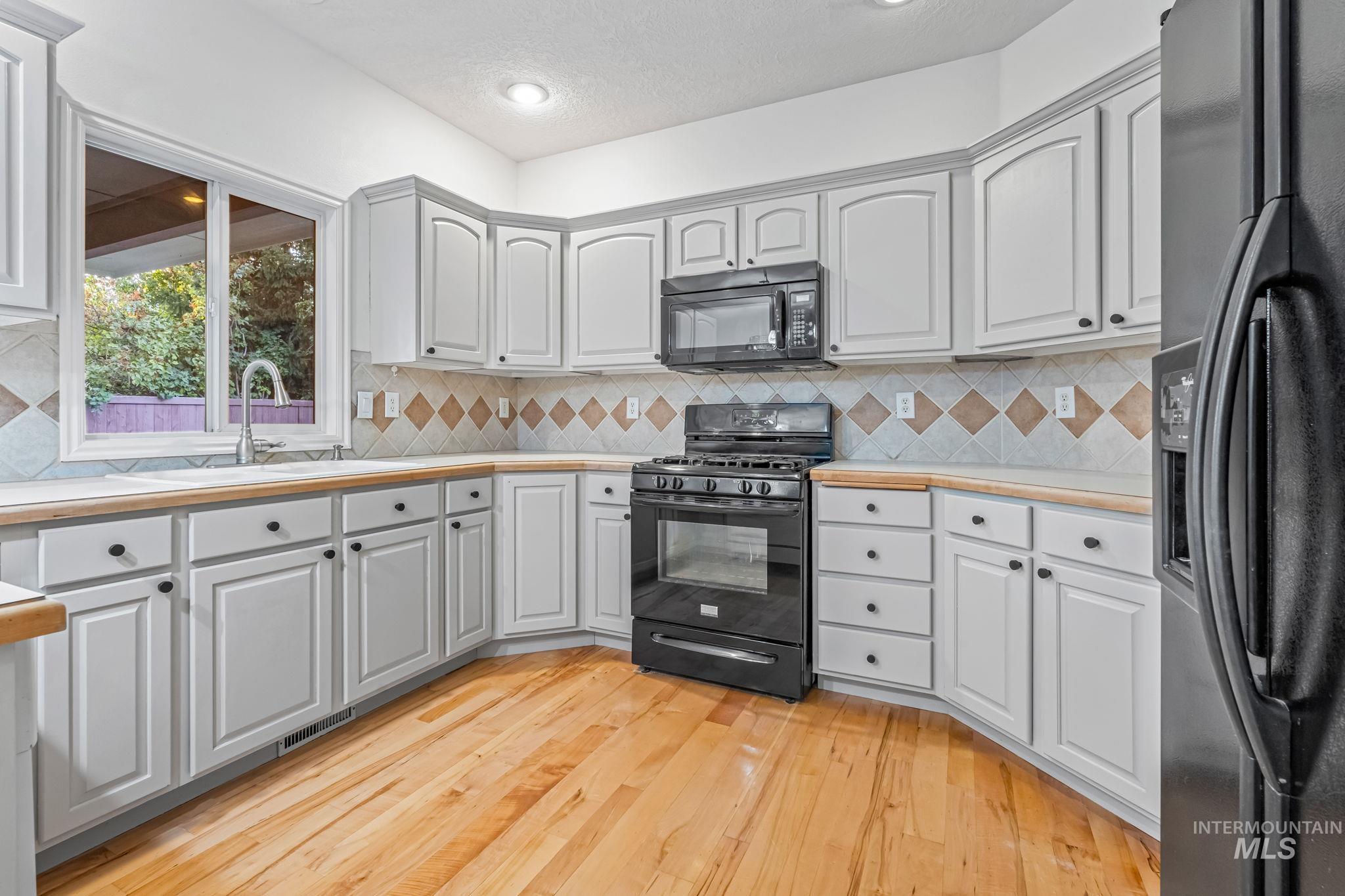 Kitchen featuring black appliances, light countertops, light wood finished floors, tasteful backsplash, and a textured ceiling