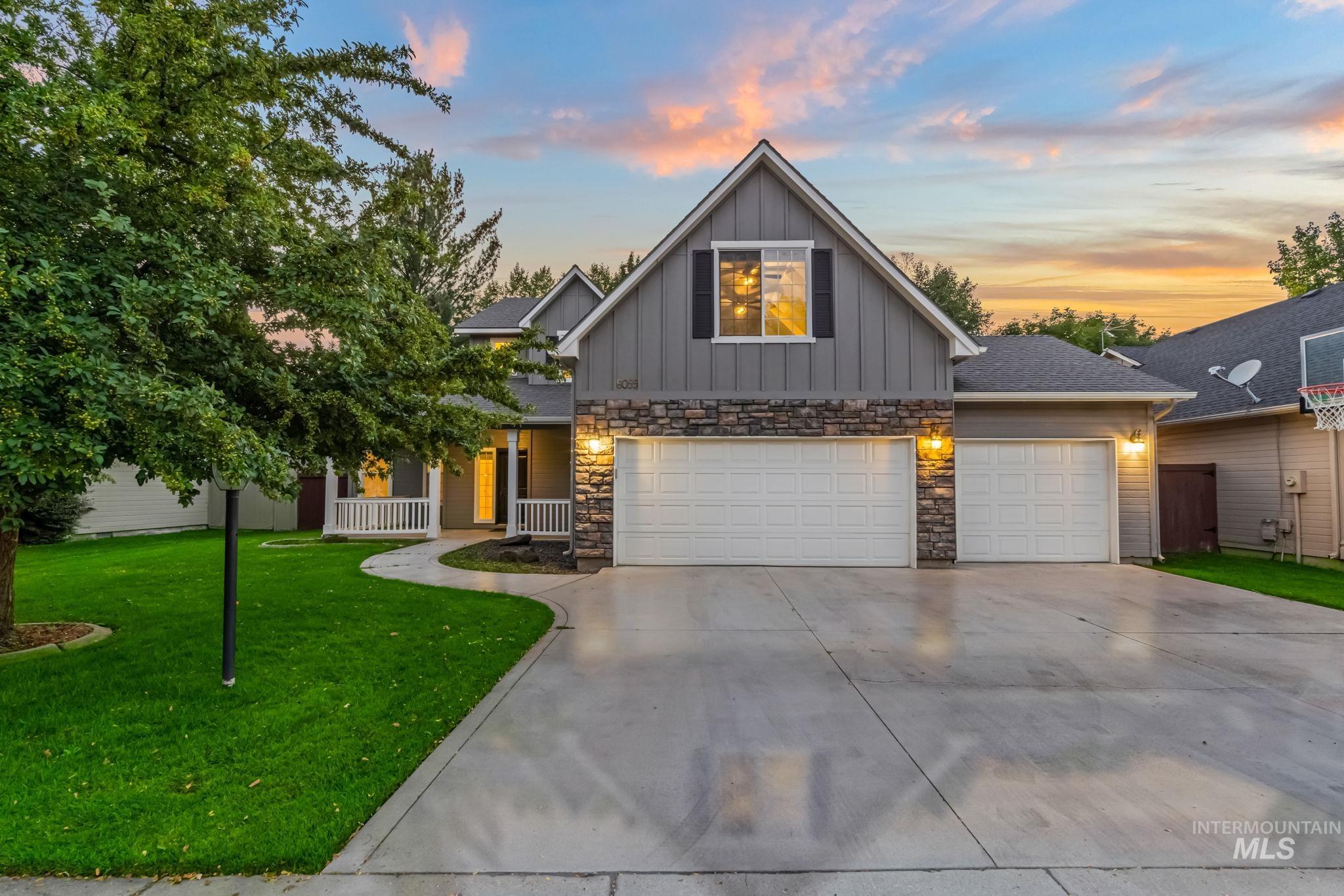 View of front of home featuring board and batten siding, a lawn, driveway, stone siding, and an attached garage
