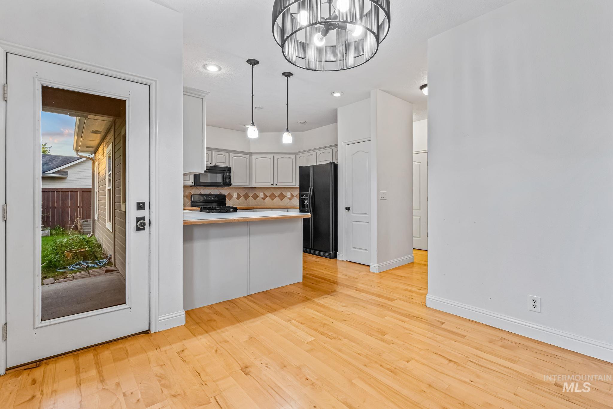Kitchen with a peninsula, white cabinetry, light countertops, pendant lighting, and backsplash