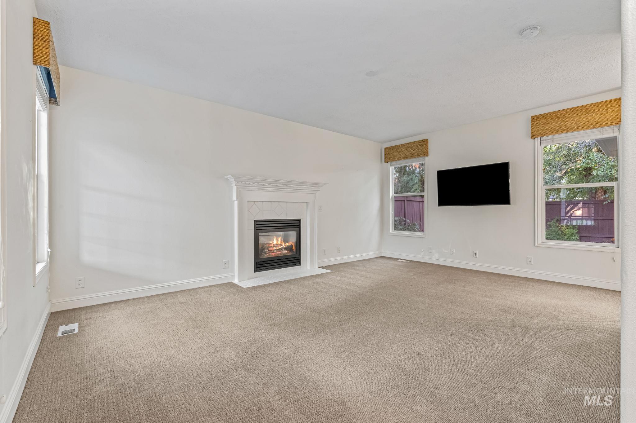 Unfurnished living room featuring carpet flooring, plenty of natural light, and a fireplace with flush hearth