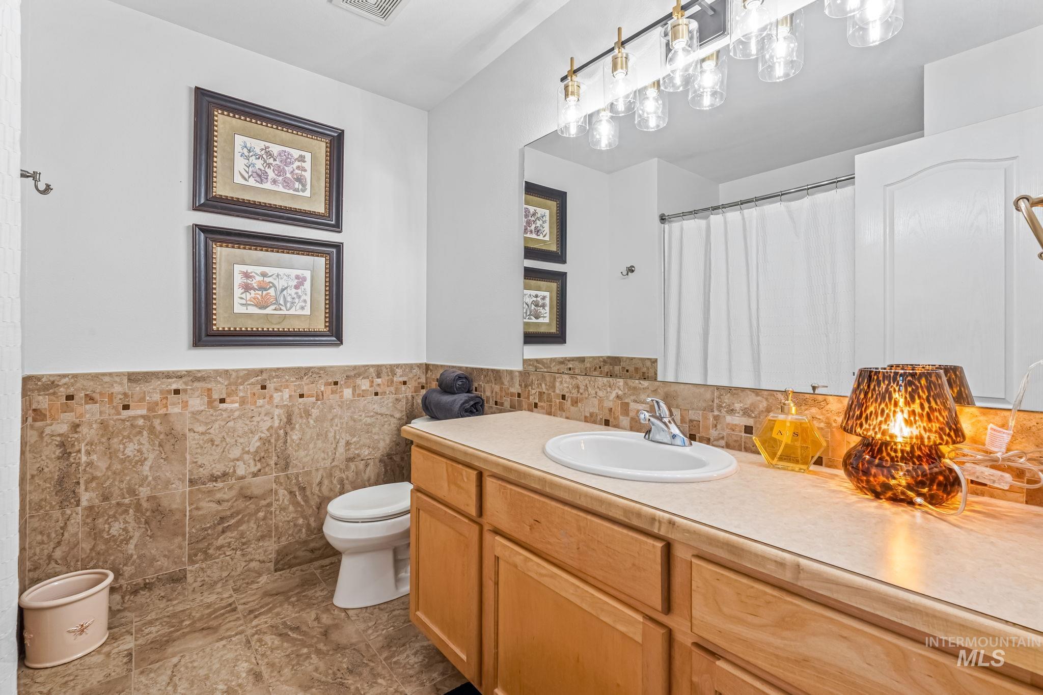 Bathroom with vanity, tile walls, curtained shower, and a wainscoted wall