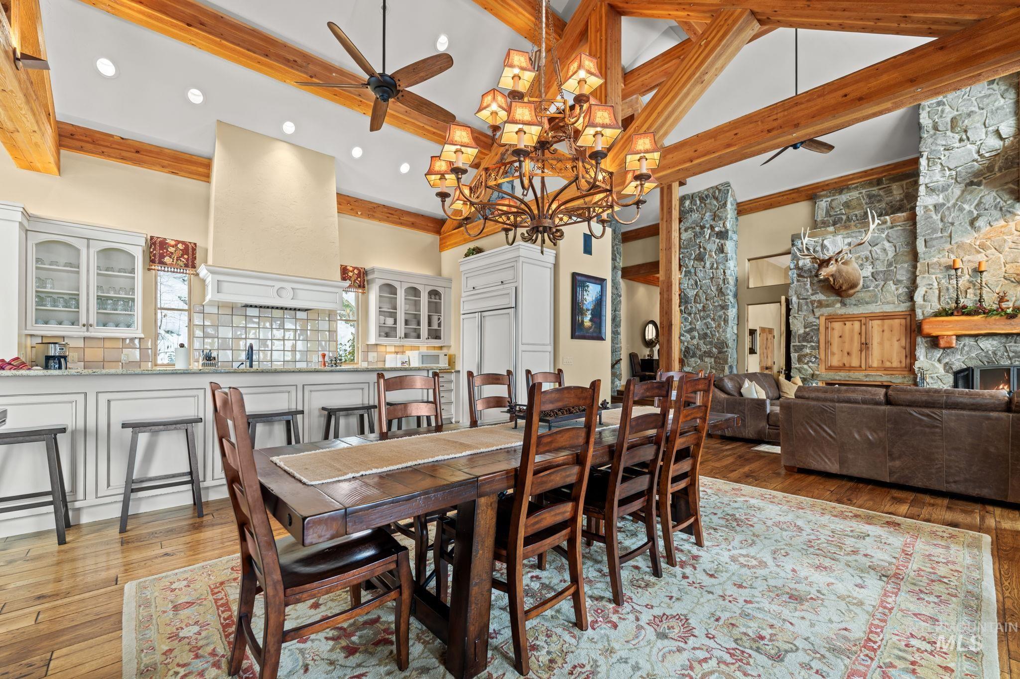 Dining area featuring high vaulted ceiling, light wood-type flooring, ceiling fan, a fireplace, and a chandelier