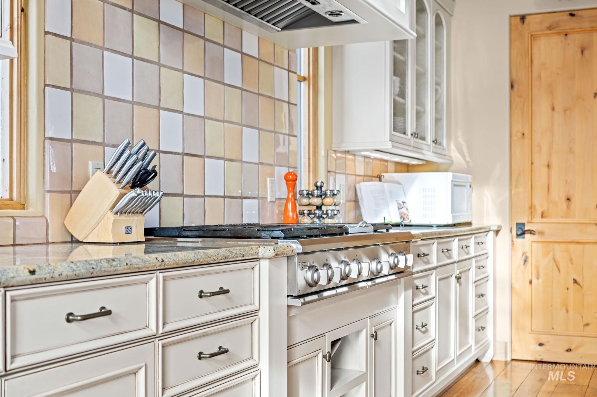 Kitchen with decorative backsplash, light stone countertops, white cabinets, ventilation hood, and stainless steel gas stovetop