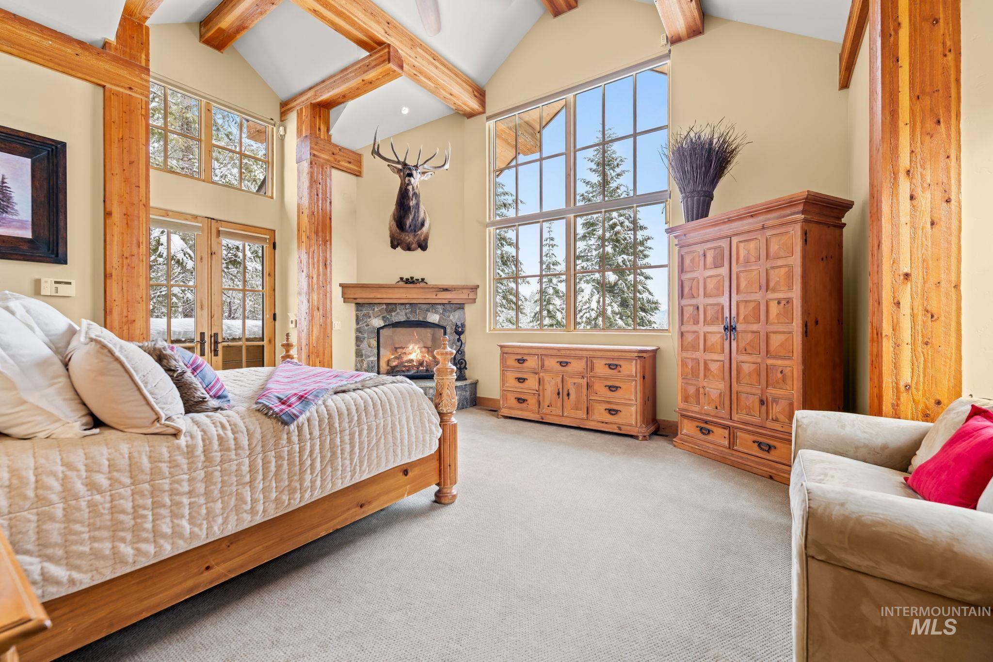 Bedroom featuring high vaulted ceiling, a stone fireplace, carpet, french doors, and beam ceiling