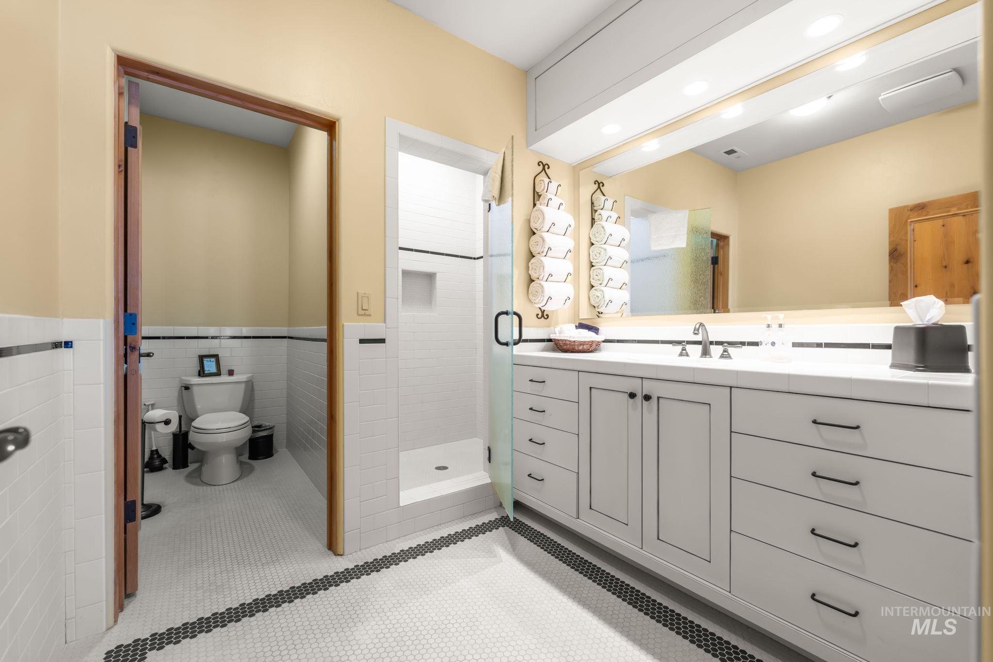 Bathroom with vanity, a stall shower, a wainscoted wall, and tile walls