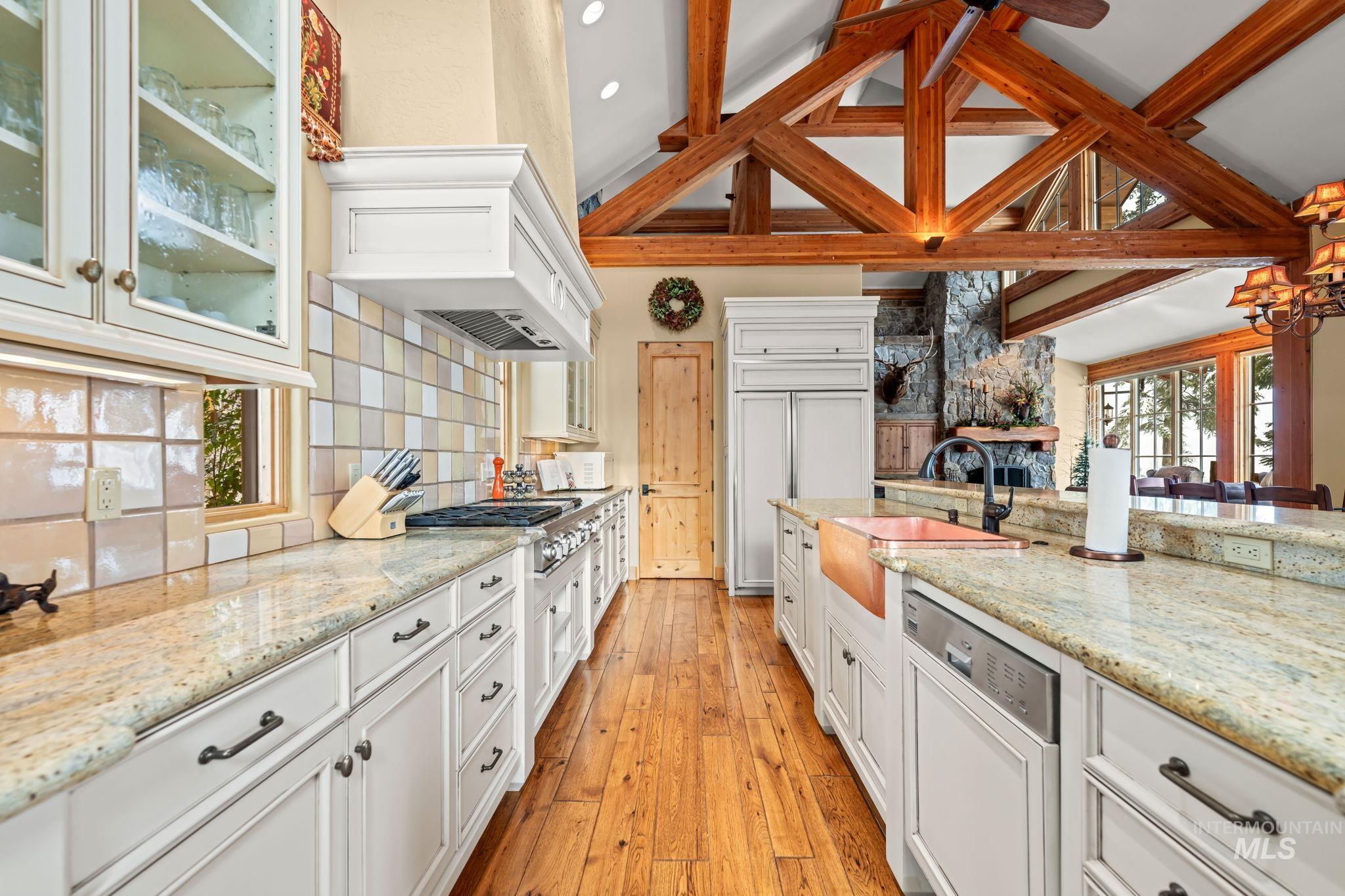 Kitchen with light stone countertops, glass insert cabinets, white cabinetry, stainless steel appliances, and lofted ceiling