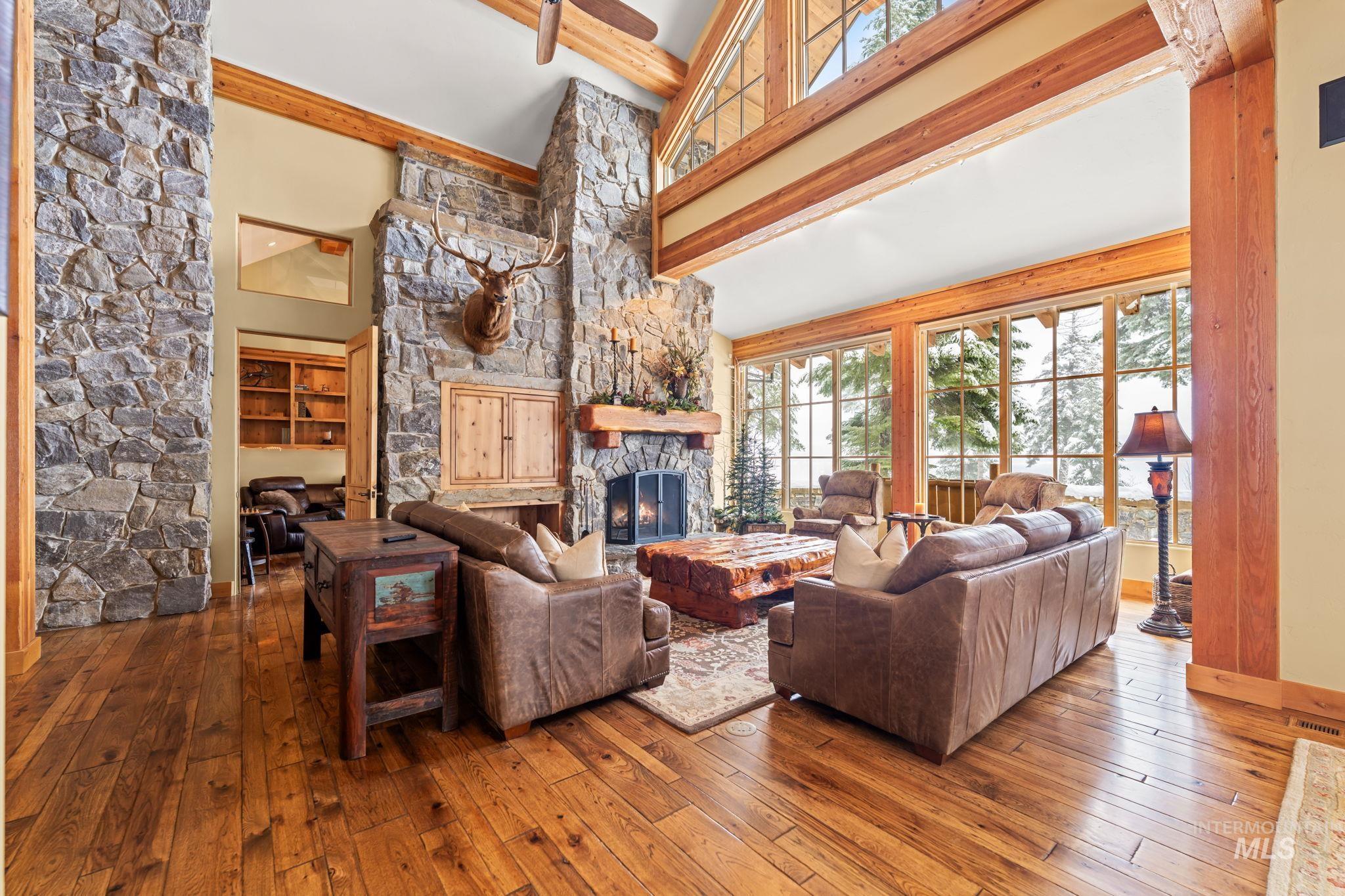 Living area with high vaulted ceiling, hardwood / wood-style floors, a stone fireplace, and beam ceiling