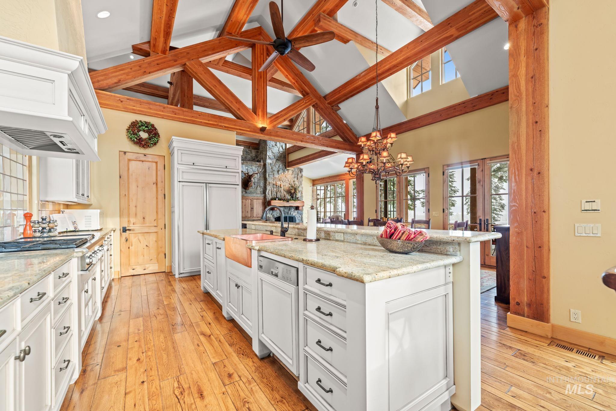 Kitchen with white cabinets, high vaulted ceiling, decorative light fixtures, light stone countertops, and light wood-style flooring