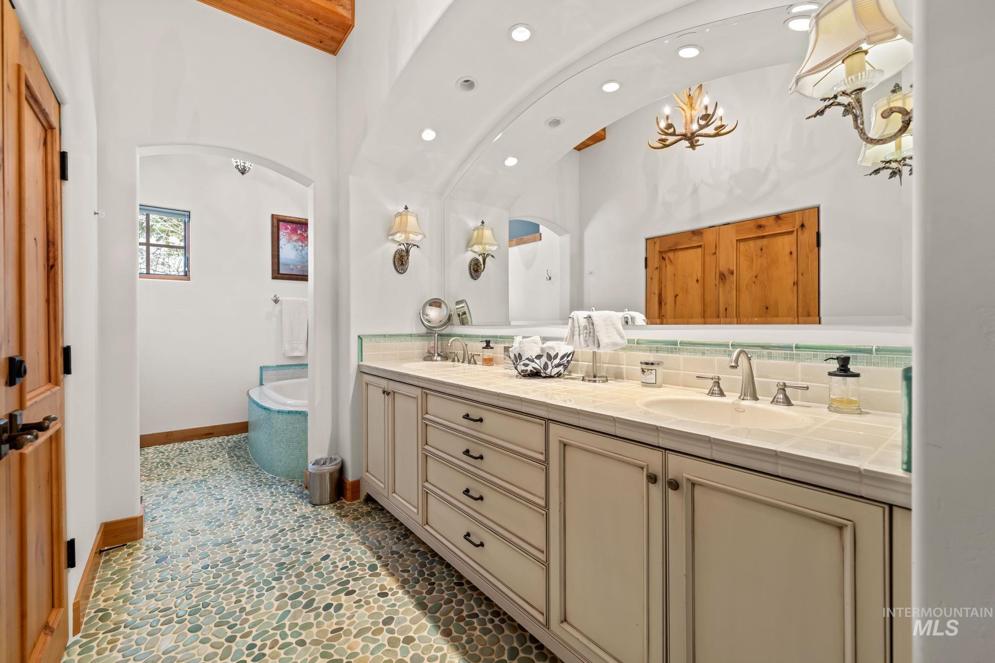 Full bath with lofted ceiling, double vanity, a bathtub, decorative backsplash, and recessed lighting