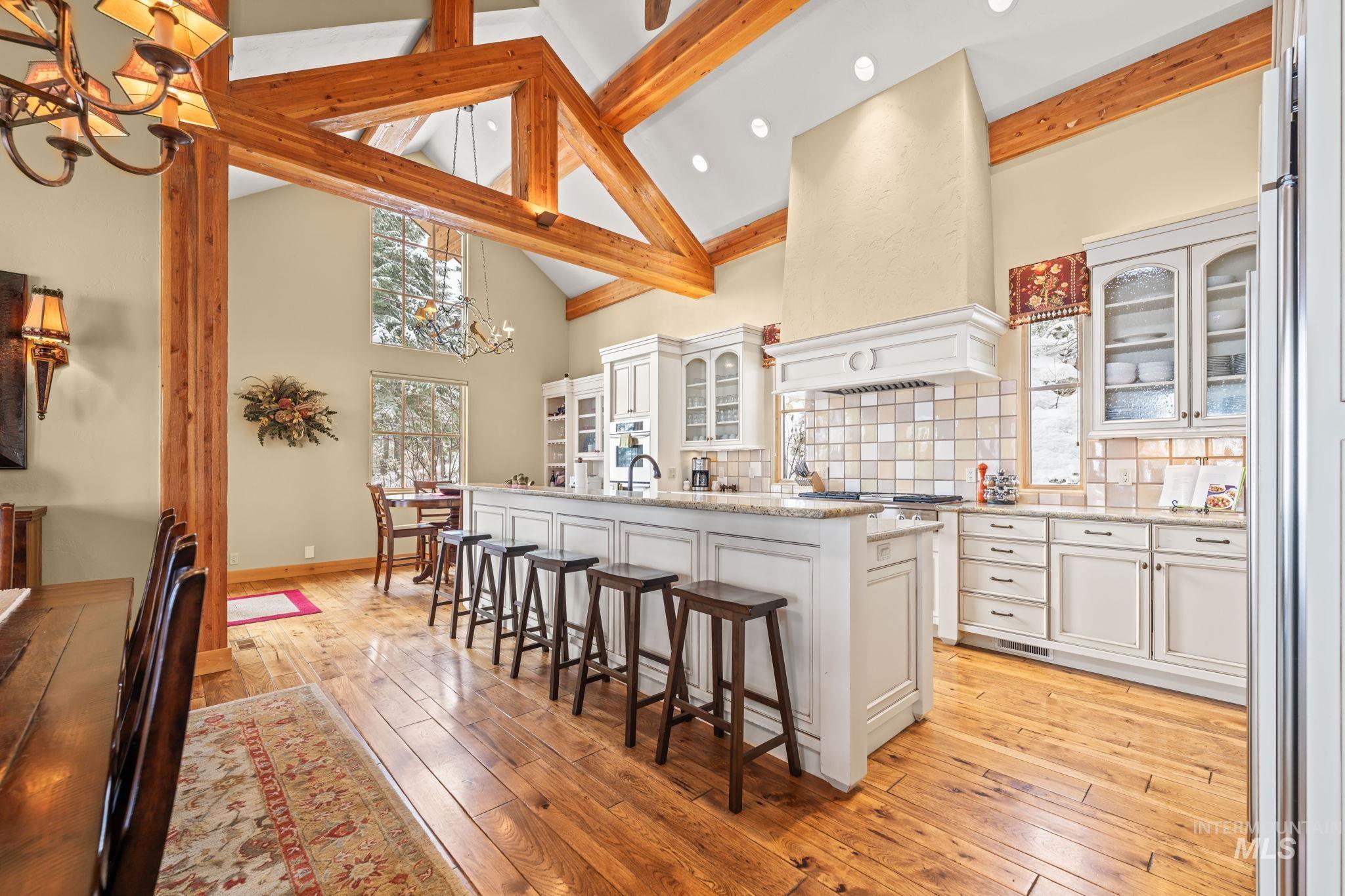 Kitchen with glass insert cabinets, a chandelier, high vaulted ceiling, decorative backsplash, and a breakfast bar