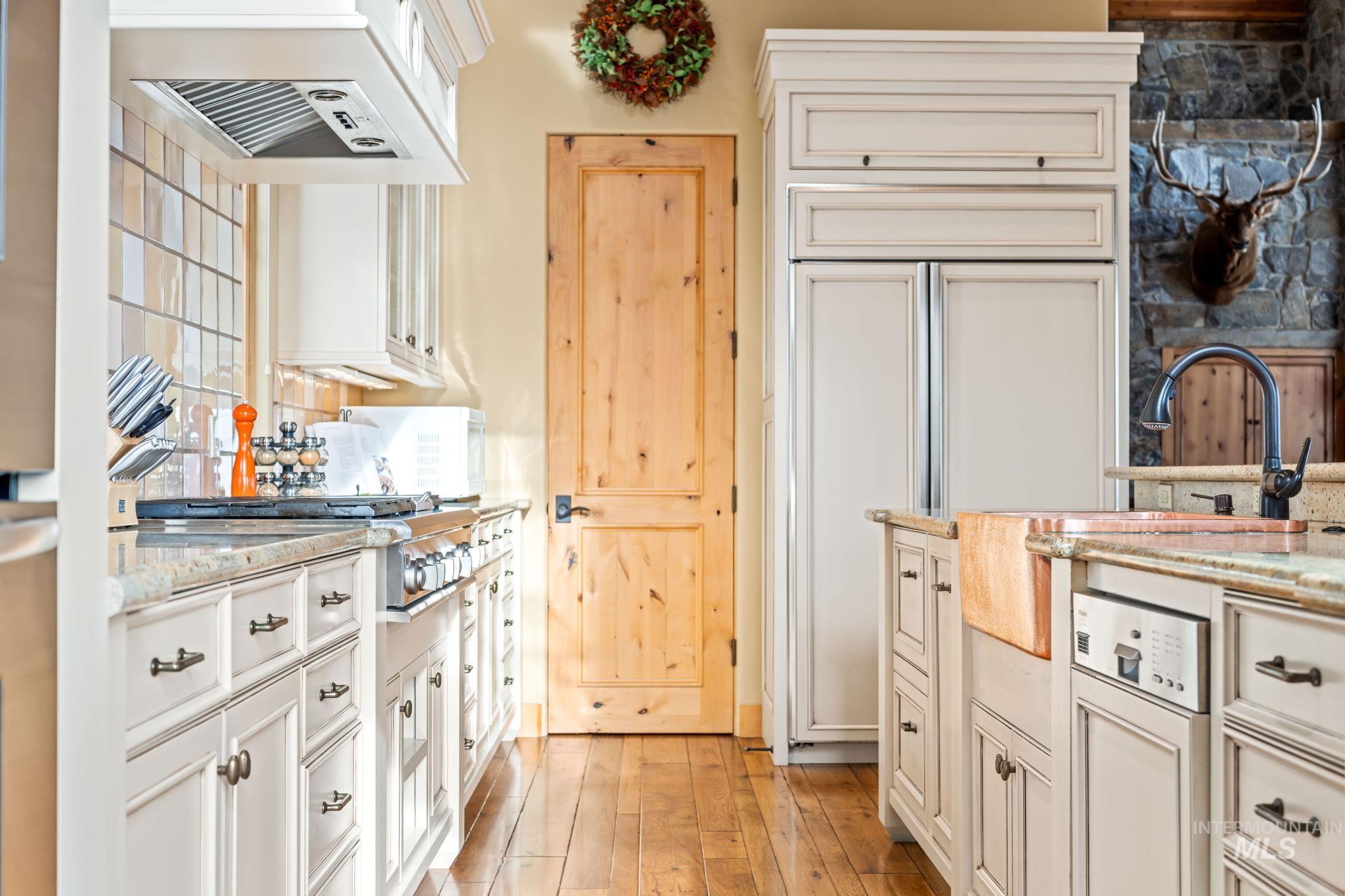Kitchen featuring light stone counters, white cabinets, under cabinet range hood, and paneled refrigerator