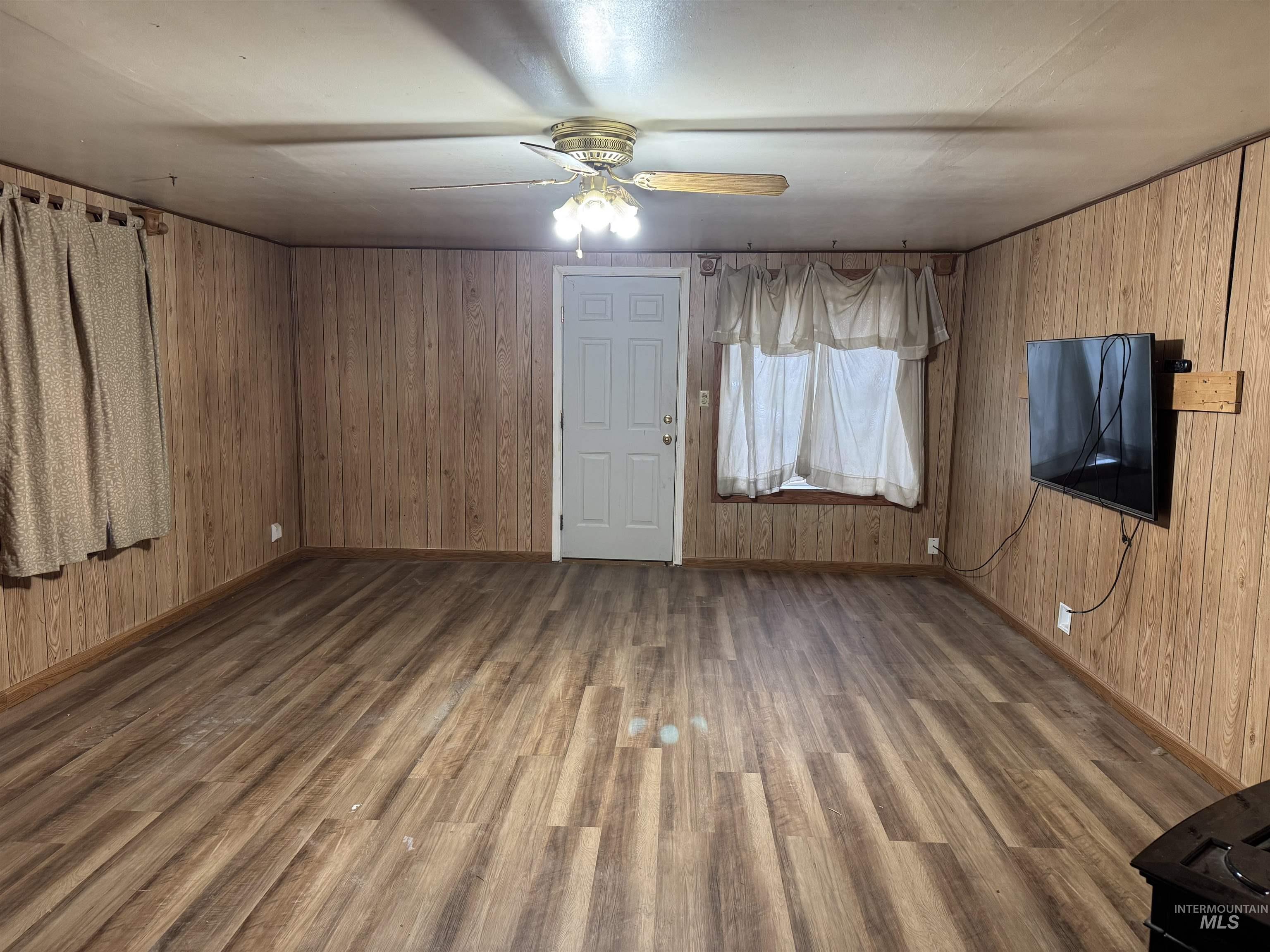 Unfurnished living room with ceiling fan, wooden walls, and dark wood-type flooring