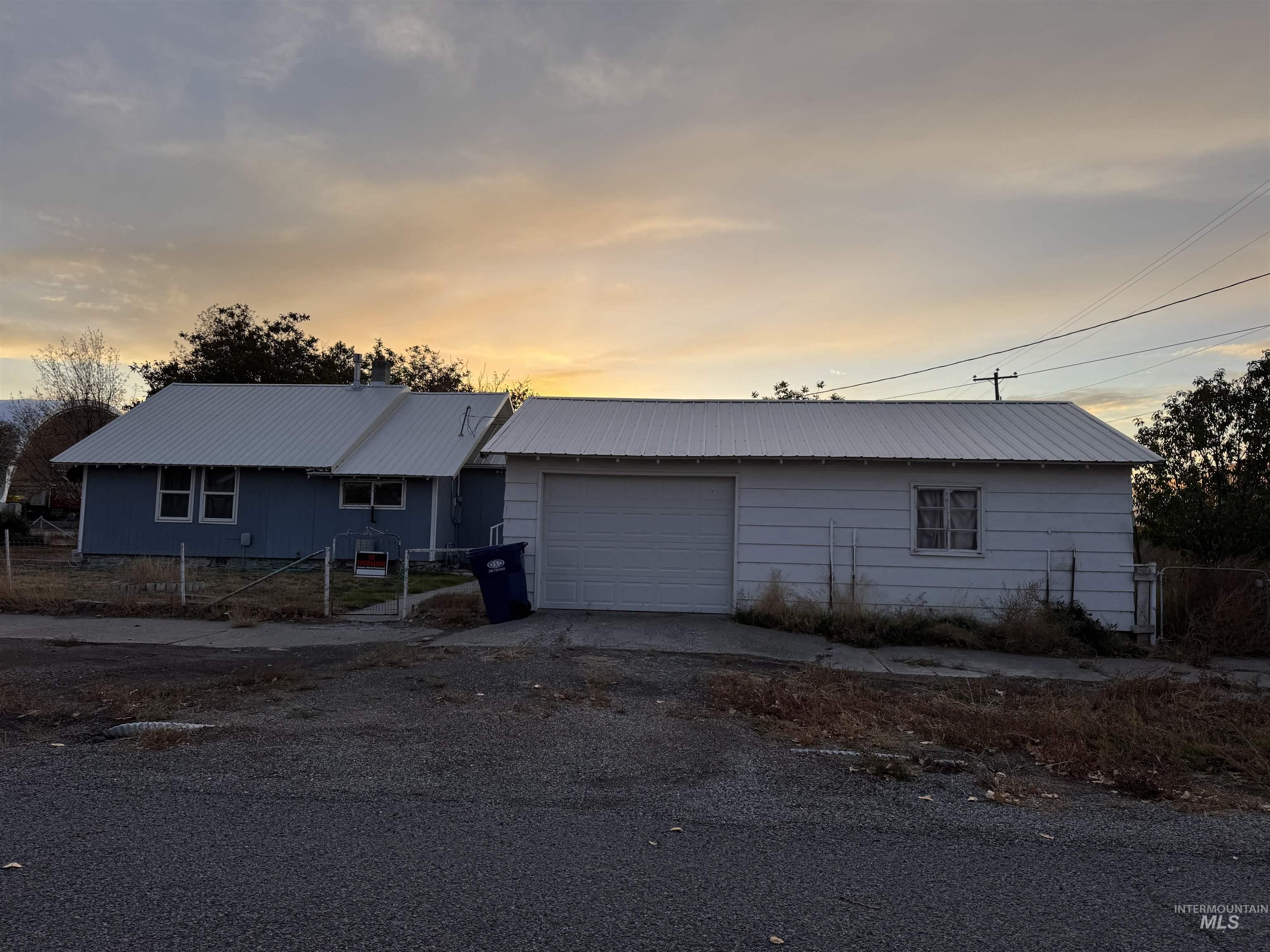 Ranch-style home with a metal roof, an attached garage, driveway, and a gate