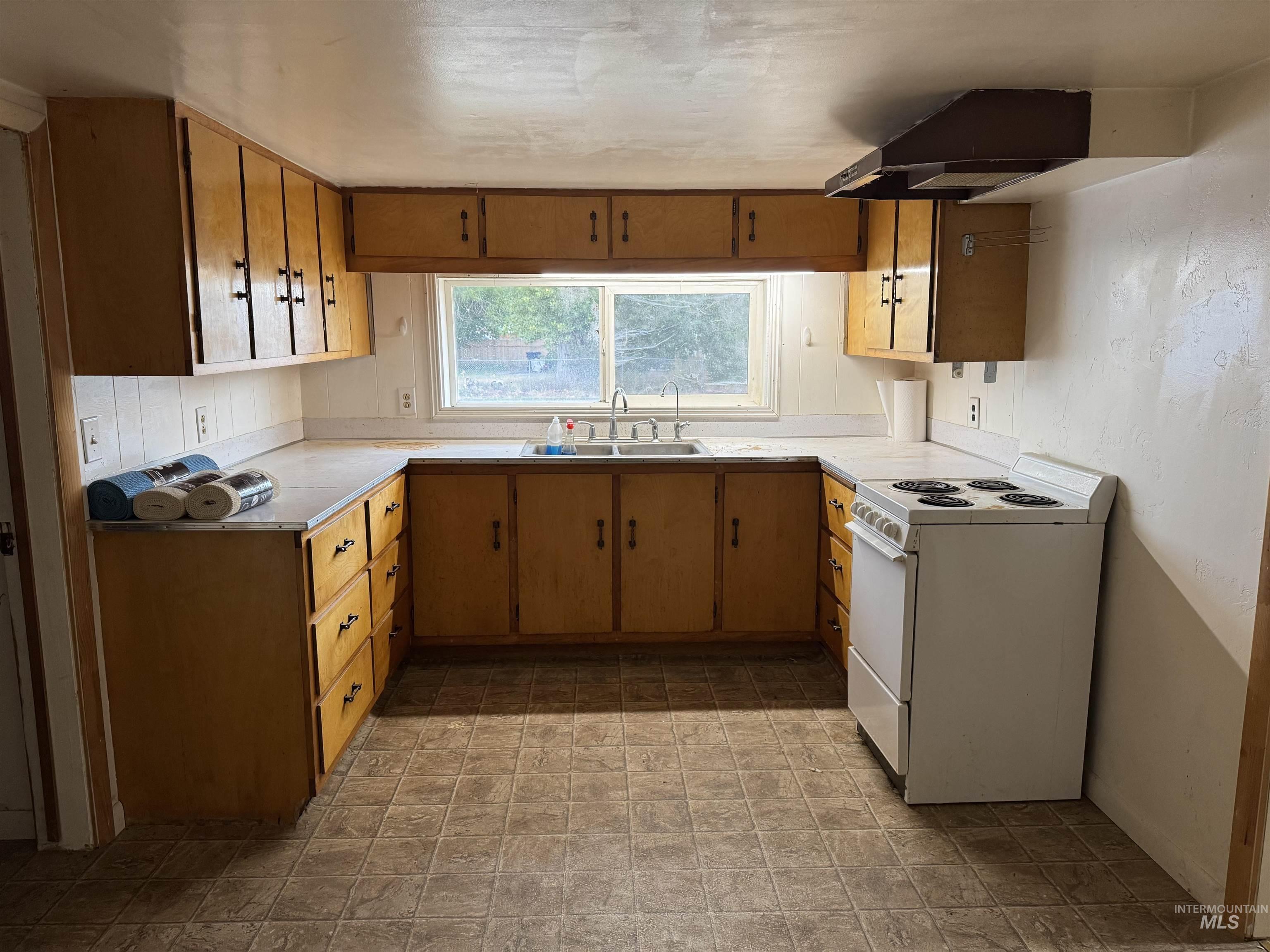 Kitchen featuring white electric stove, light countertops, range hood, and brown cabinetry