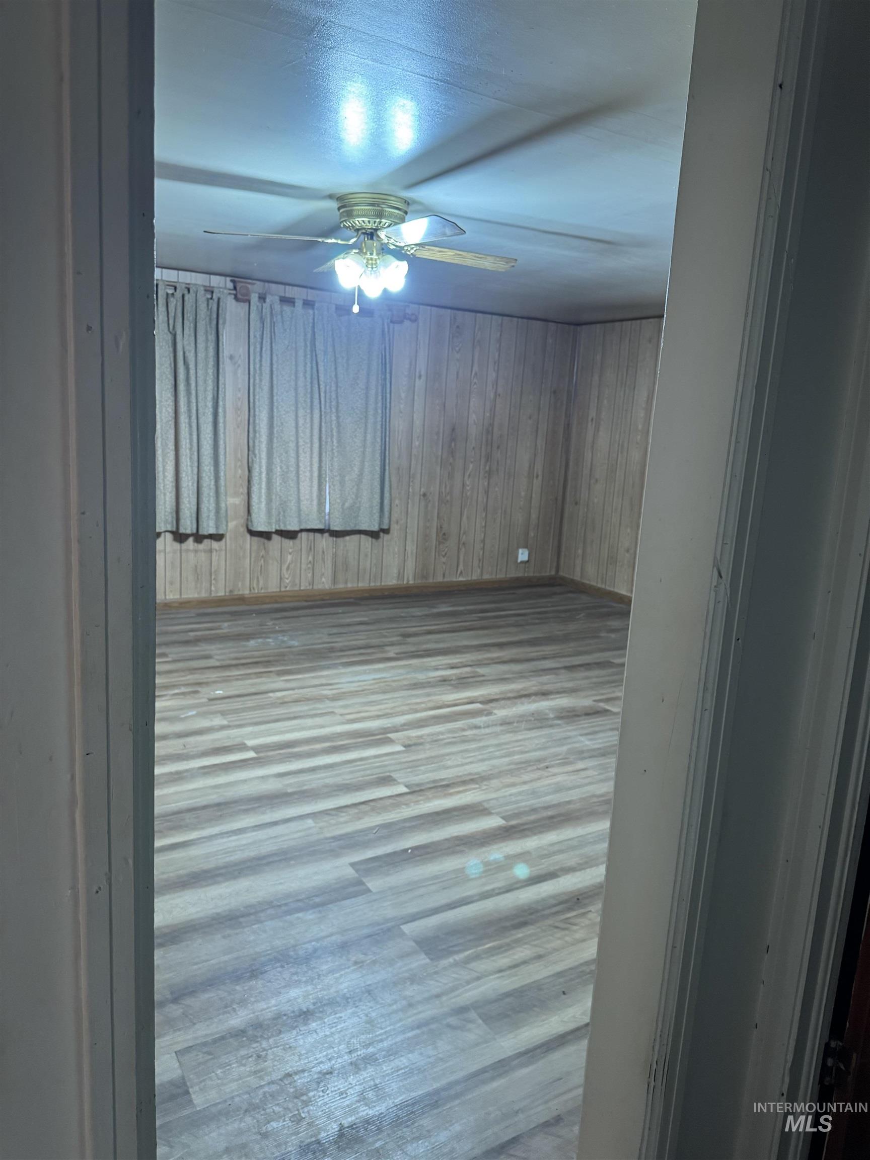 Empty room featuring wood finished floors, wood walls, and ceiling fan