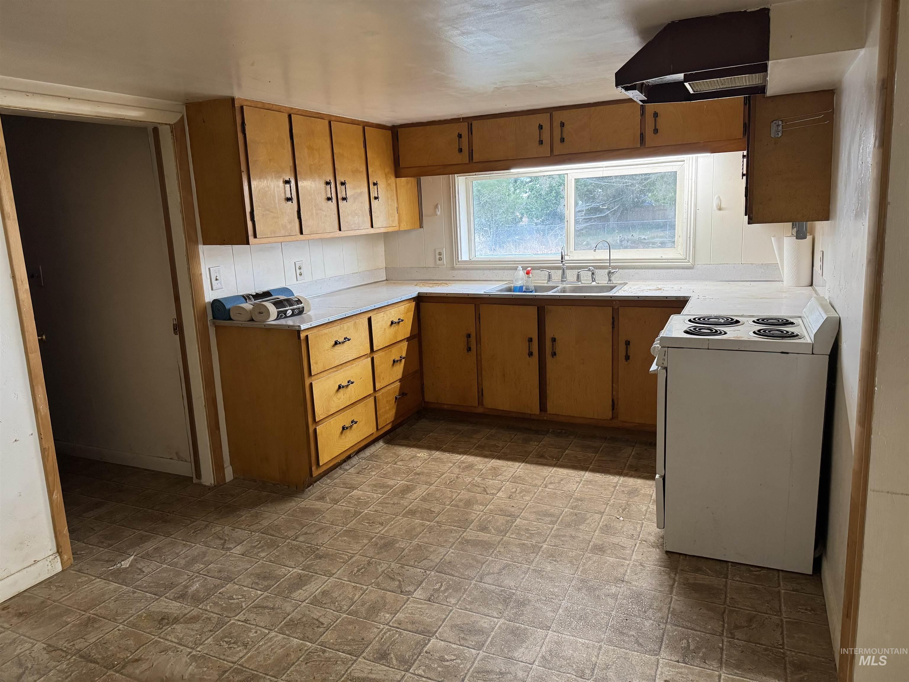 Kitchen featuring white electric range, light countertops, brown cabinetry, and extractor fan