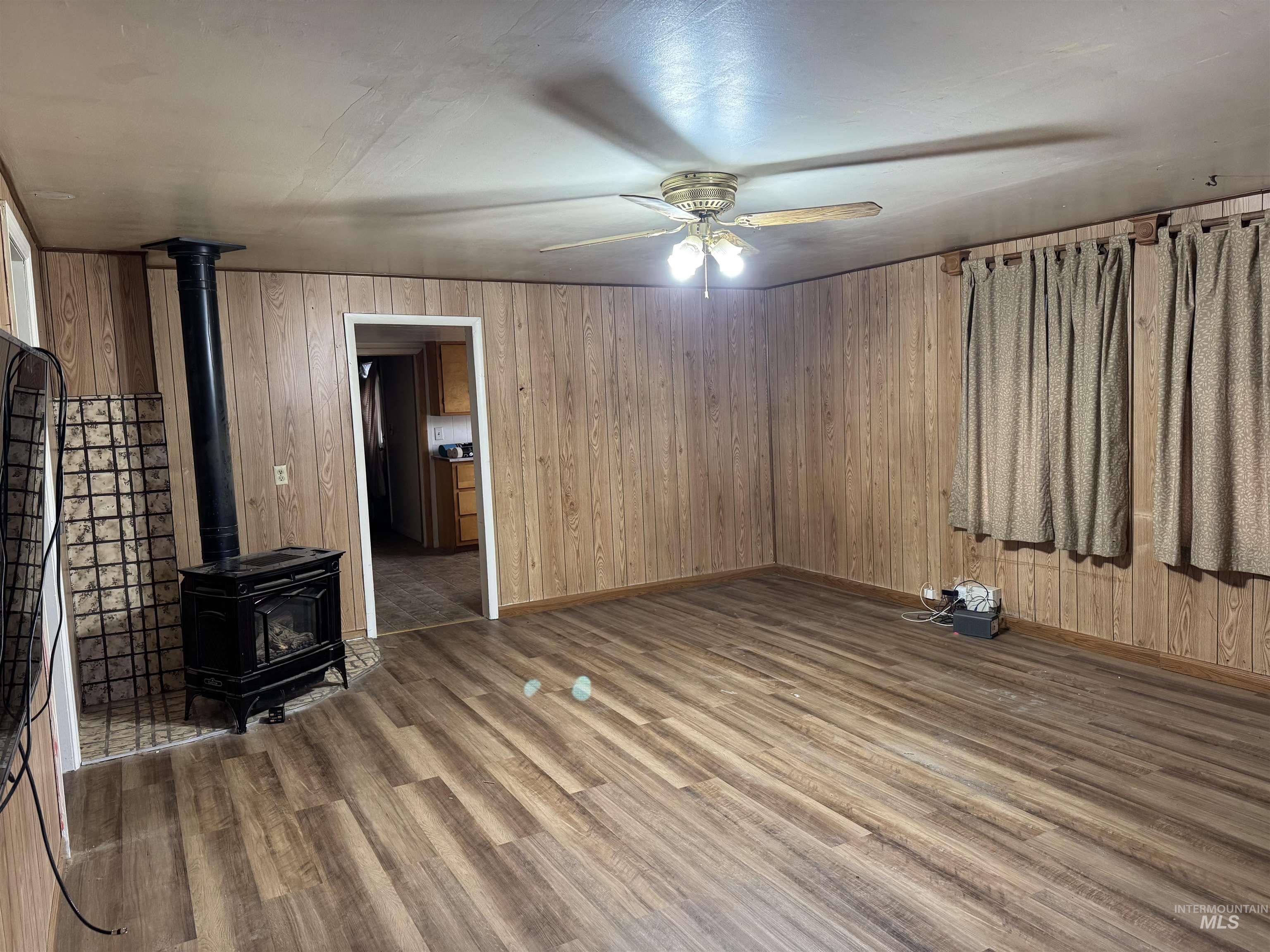 Unfurnished living room with a wood stove, wood walls, wood finished floors, and ceiling fan