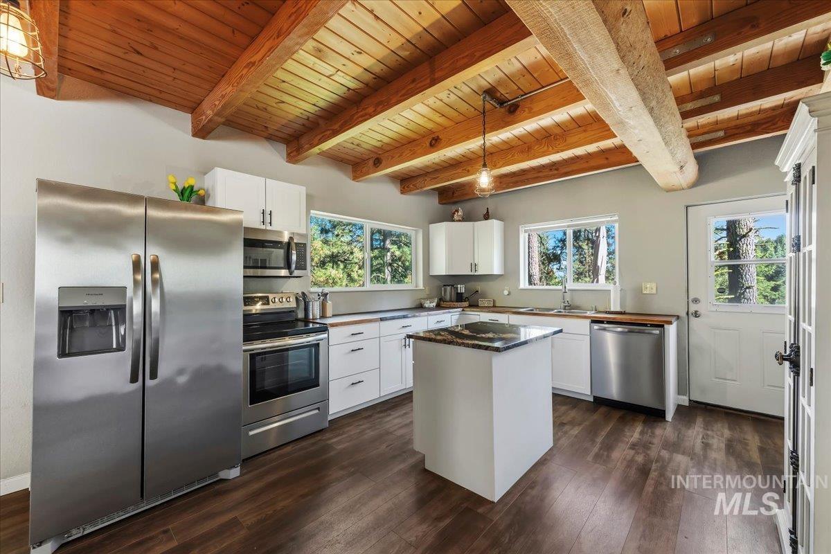 Open-concept kitchen featuring vaulted wood plank ceilings with exposed beams, stainless steel appliances, a center island with a granite countertop, wood-finish flooring, and white cabinetry