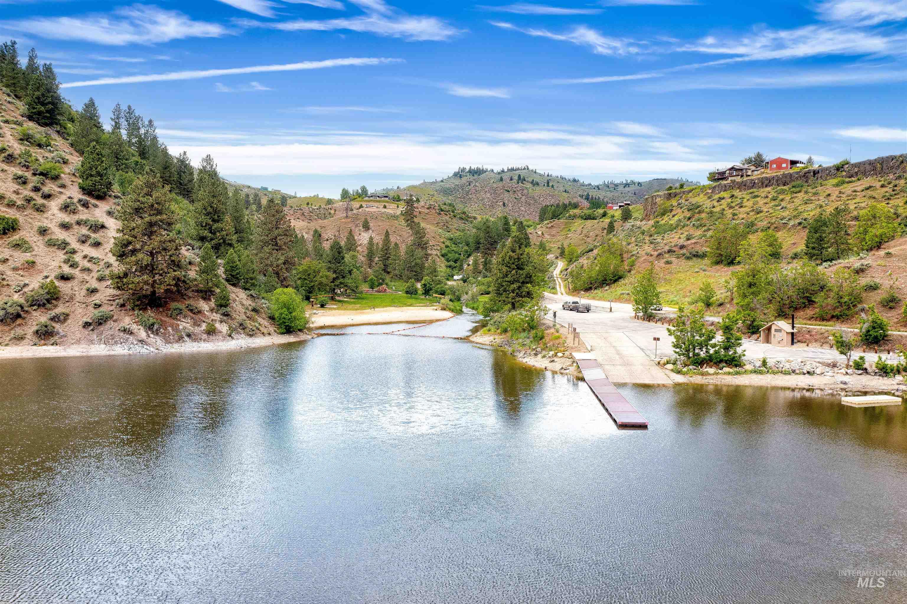 Waterfront property featuring a boat launch, dock, and surrounding natural landscape with mature trees and rolling hills