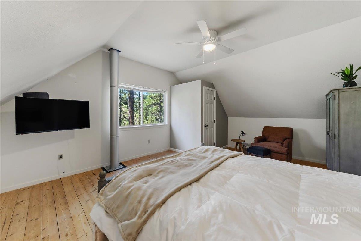 Attic bedroom featuring pitched ceilings, wood-finish flooring, and a ceiling fan