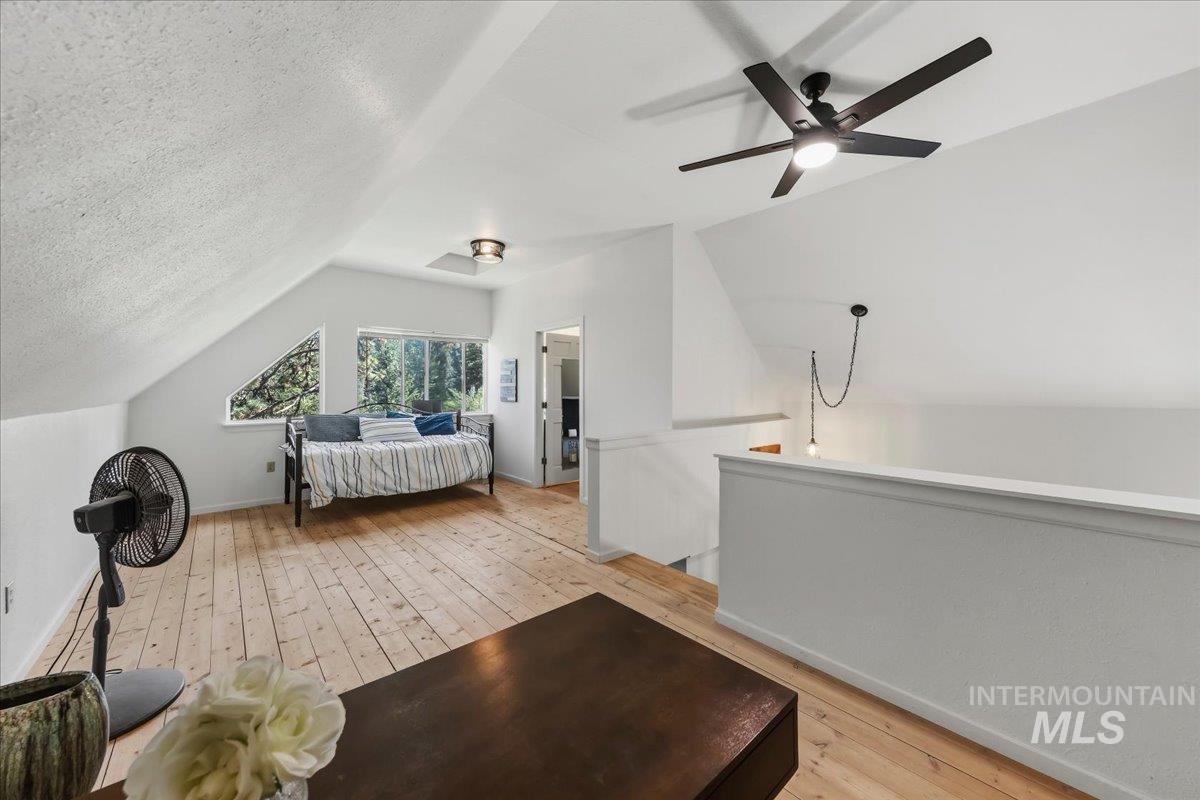 Spacious loft area featuring light wood-finish flooring, a contemporary ceiling fan with integrated lighting, and multiple windows