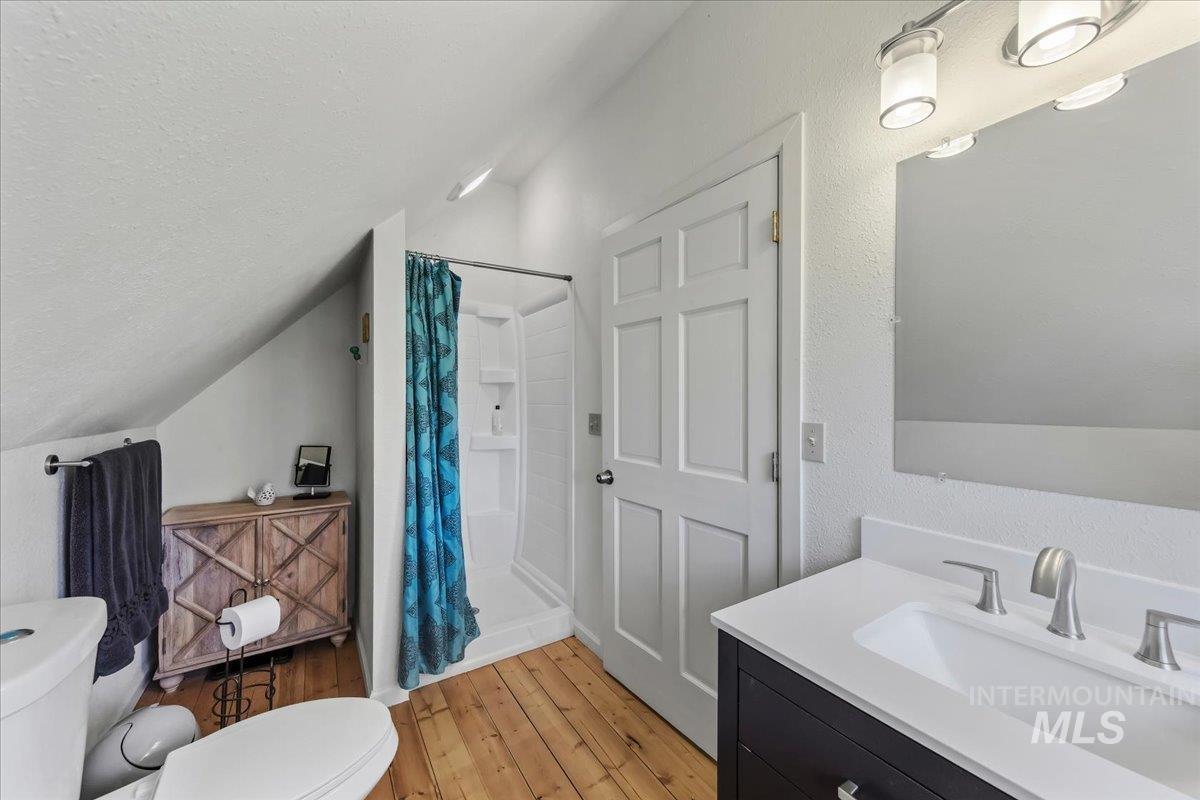 Bathroom featuring a single-basin vanity with a white countertop, wood-finish flooring, a white paneled door, and a shower stall
