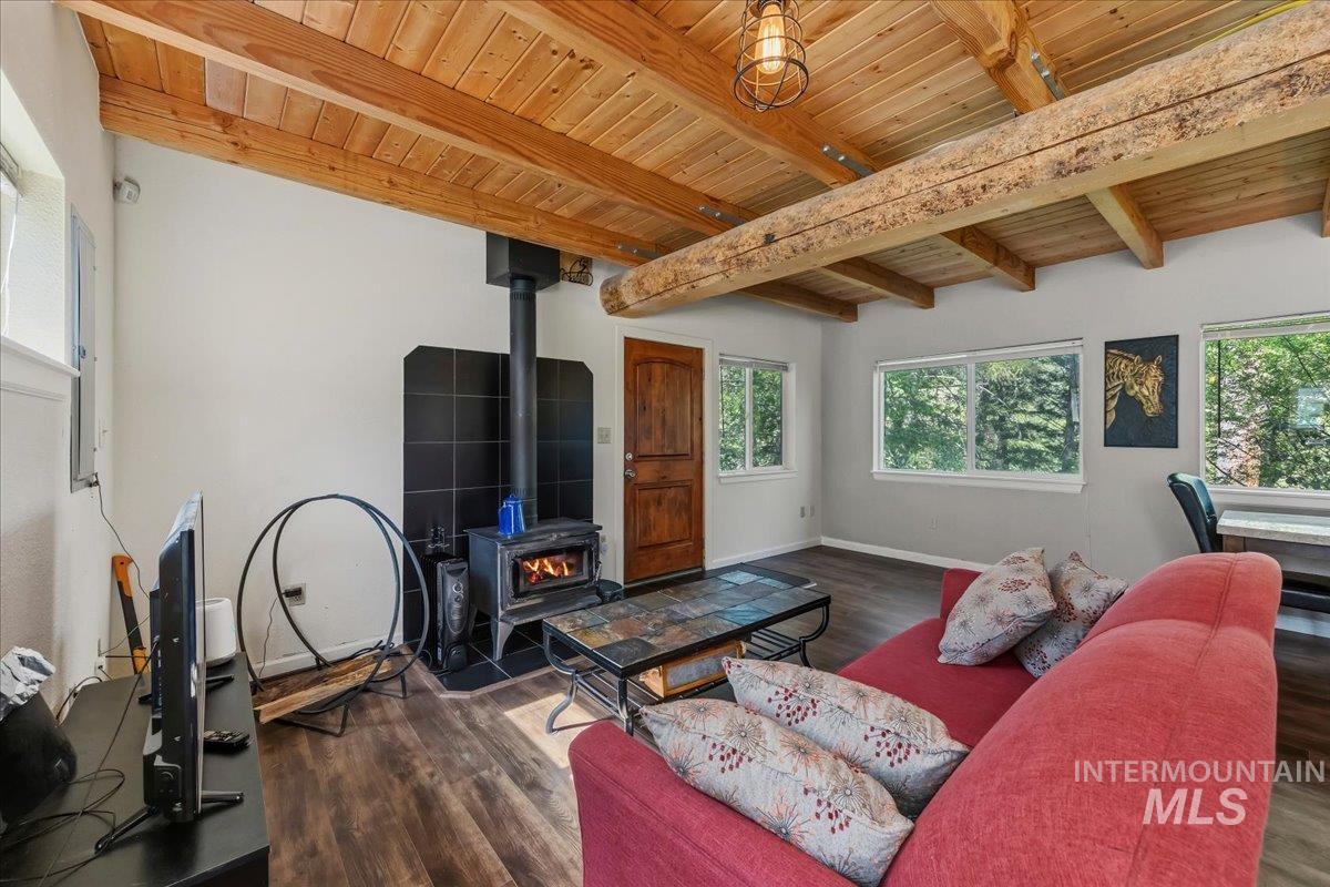 Warm living space featuring a wood-burning stove with a black tile surround, wood-finish flooring, and exposed timber ceiling beams