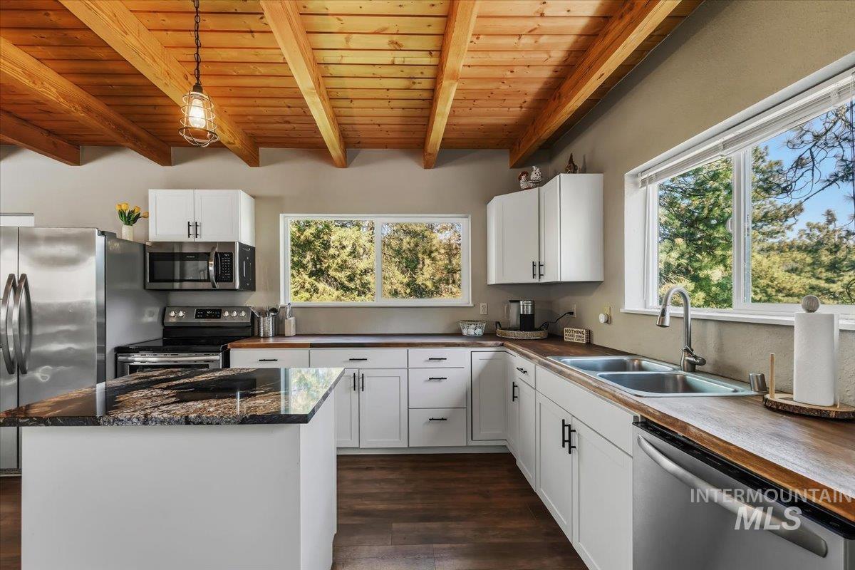 Kitchen featuring an exposed wood beam ceiling, white cabinetry, dark wood-finish flooring, a central island with a dark stone countertop, and stainless steel appliances