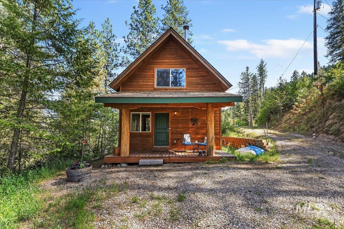 Wood-sided cabin featuring a covered front porch with log columns, a dark green entry door, and a gravel driveway