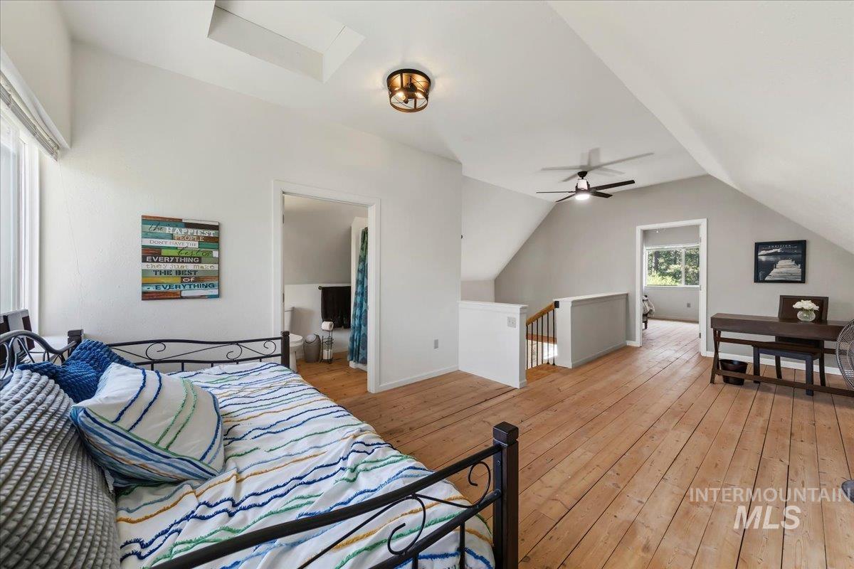 Spacious upper-level room featuring wood-finish flooring, a vaulted ceiling, a skylight, and an attached ceiling fan