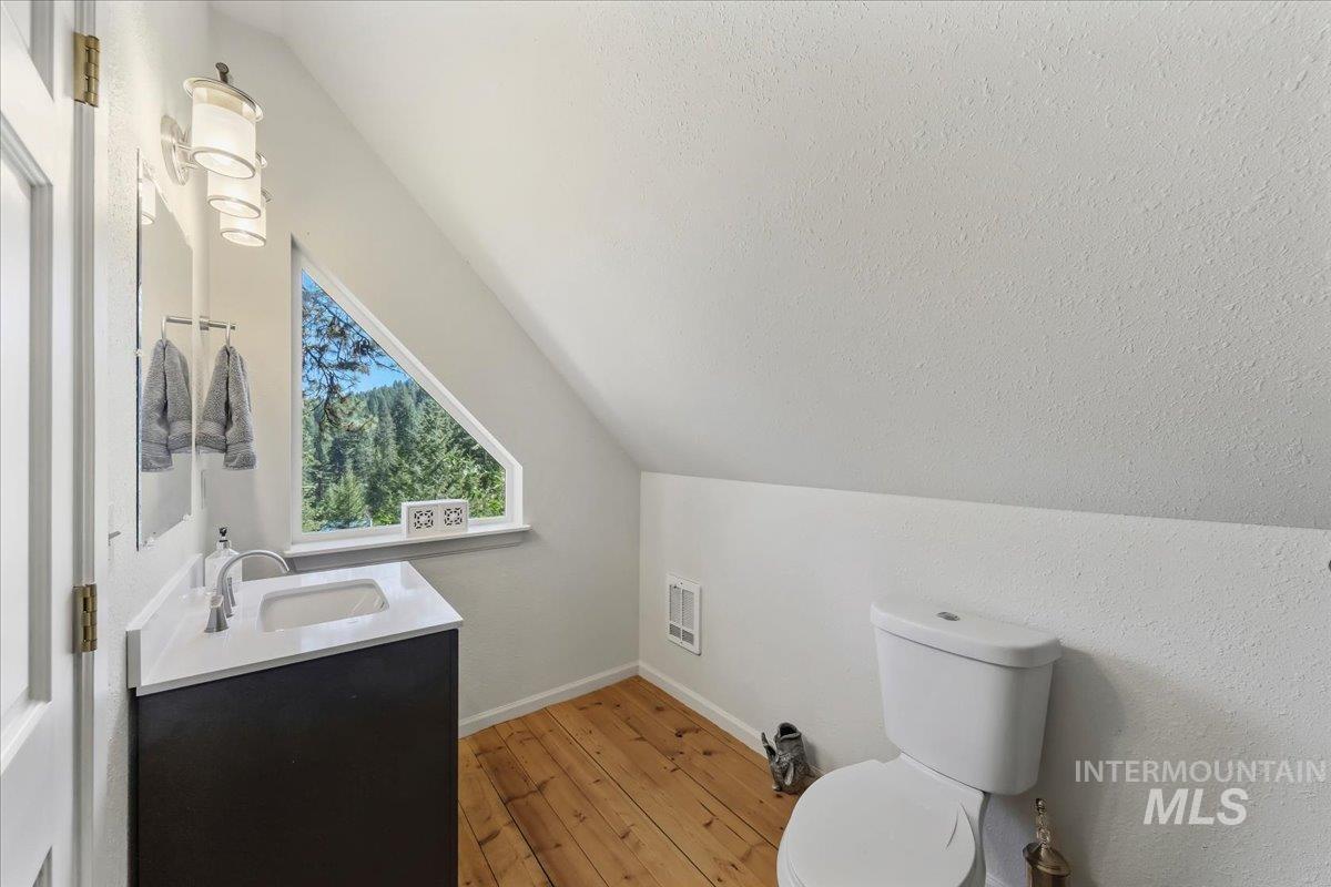 Bathroom featuring a contemporary vanity with a white countertop, a unique triangular window, wood-finish flooring, and a wall-mounted light fixture