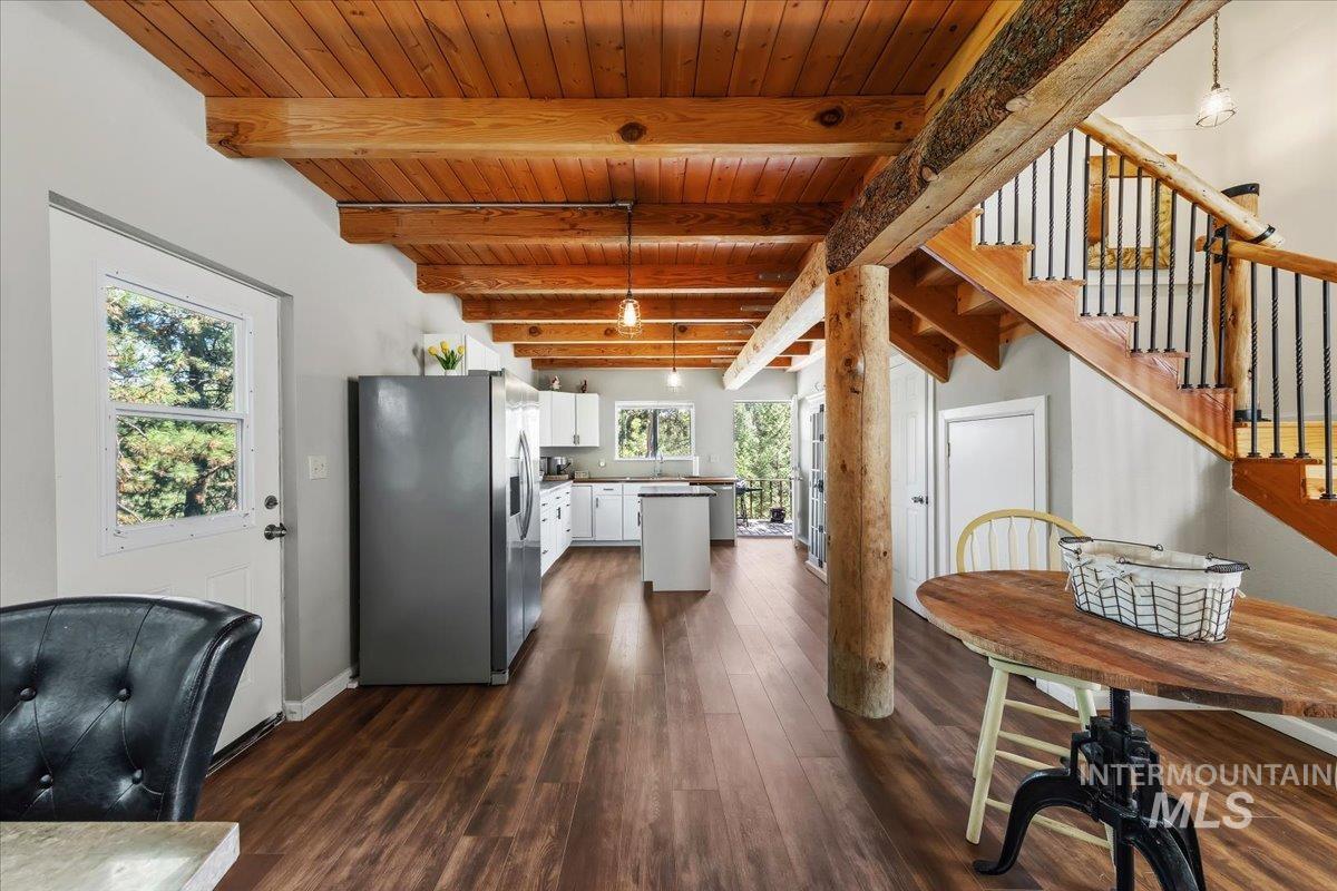Open-concept kitchen and living area featuring exposed wood beam ceilings, wood-finish flooring, a white kitchen with stainless steel appliances, and a wood staircase with wrought iron balusters