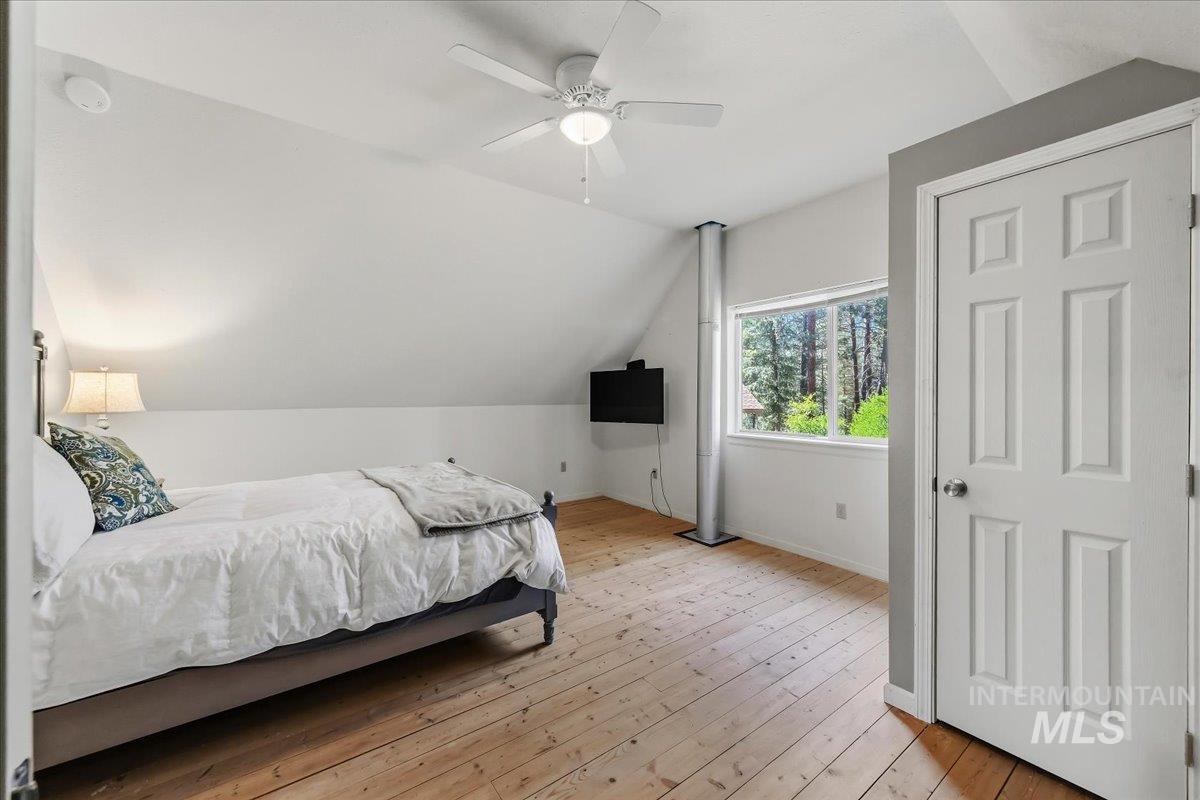 Attic bedroom featuring vaulted ceilings, wood-finish flooring, and a multi-pane window