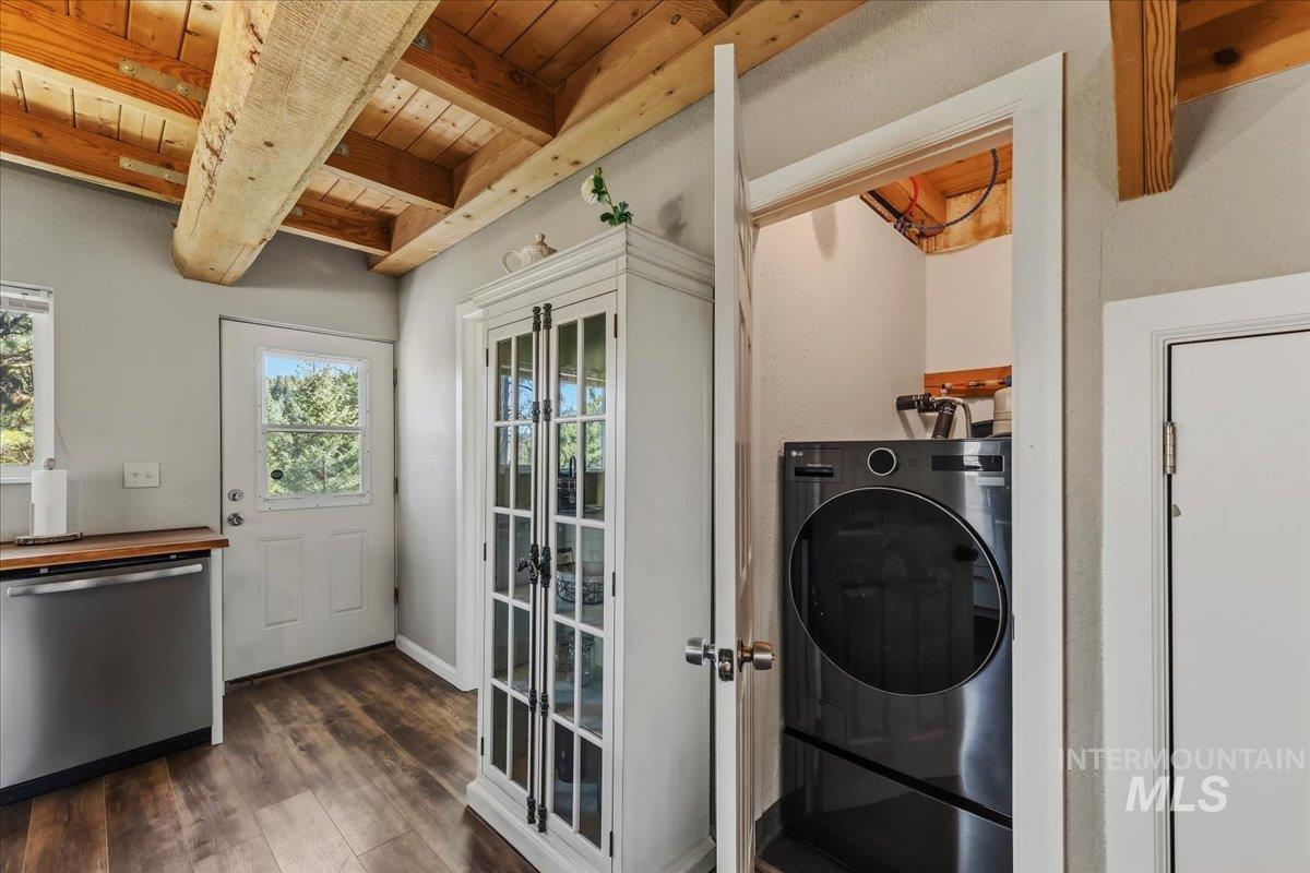 Laundry nook featuring a stacked washer and dryer, wood-finish flooring, exposed wood beams, a white glass-paneled cabinet, and a white exterior door with glass insert