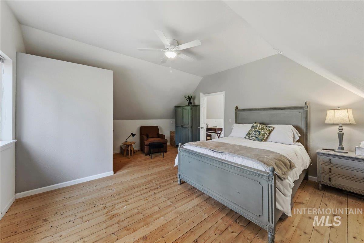 Vaulted ceiling with a ceiling fan, light wood-finish flooring, white baseboards, and a window with white trim