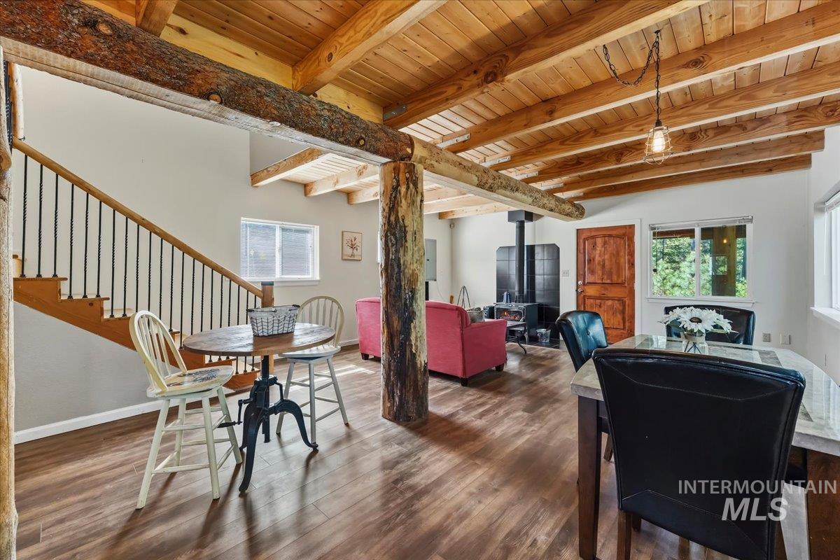 Open-concept living space featuring wood-finish flooring, exposed timber beams, a central wood-burning stove, and a wood staircase with iron balusters