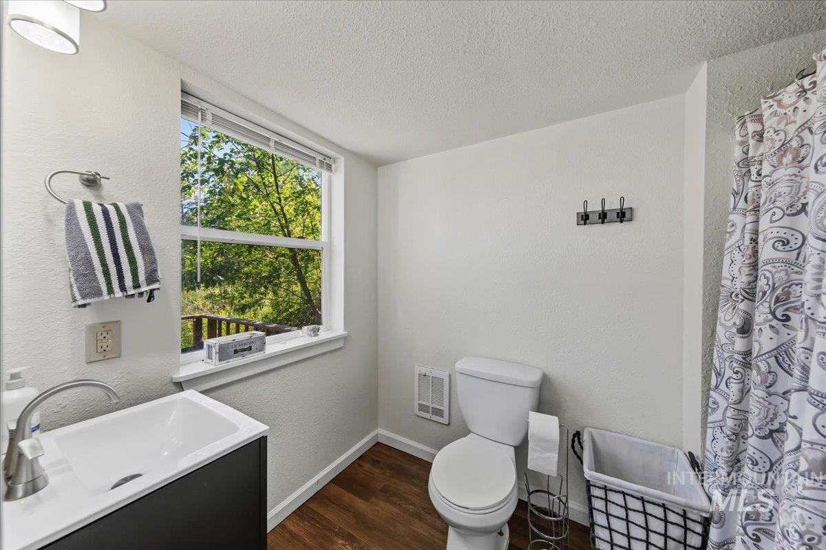 Contemporary bathroom featuring wood-finish flooring, a white vanity with an integrated sink, a toilet, and a window with blinds