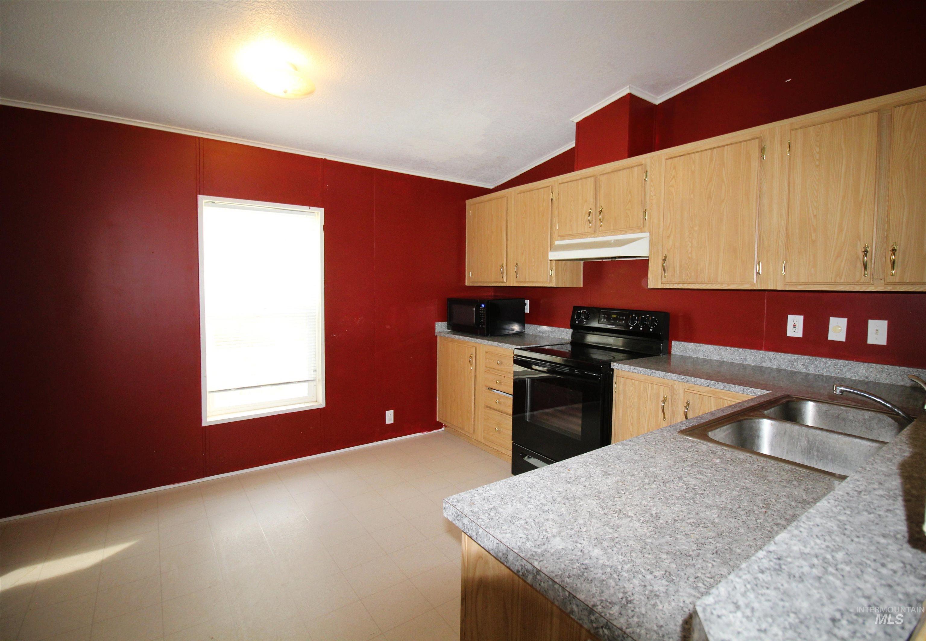 Kitchen with light brown cabinetry, black appliances, light floors, crown molding, and vaulted ceiling