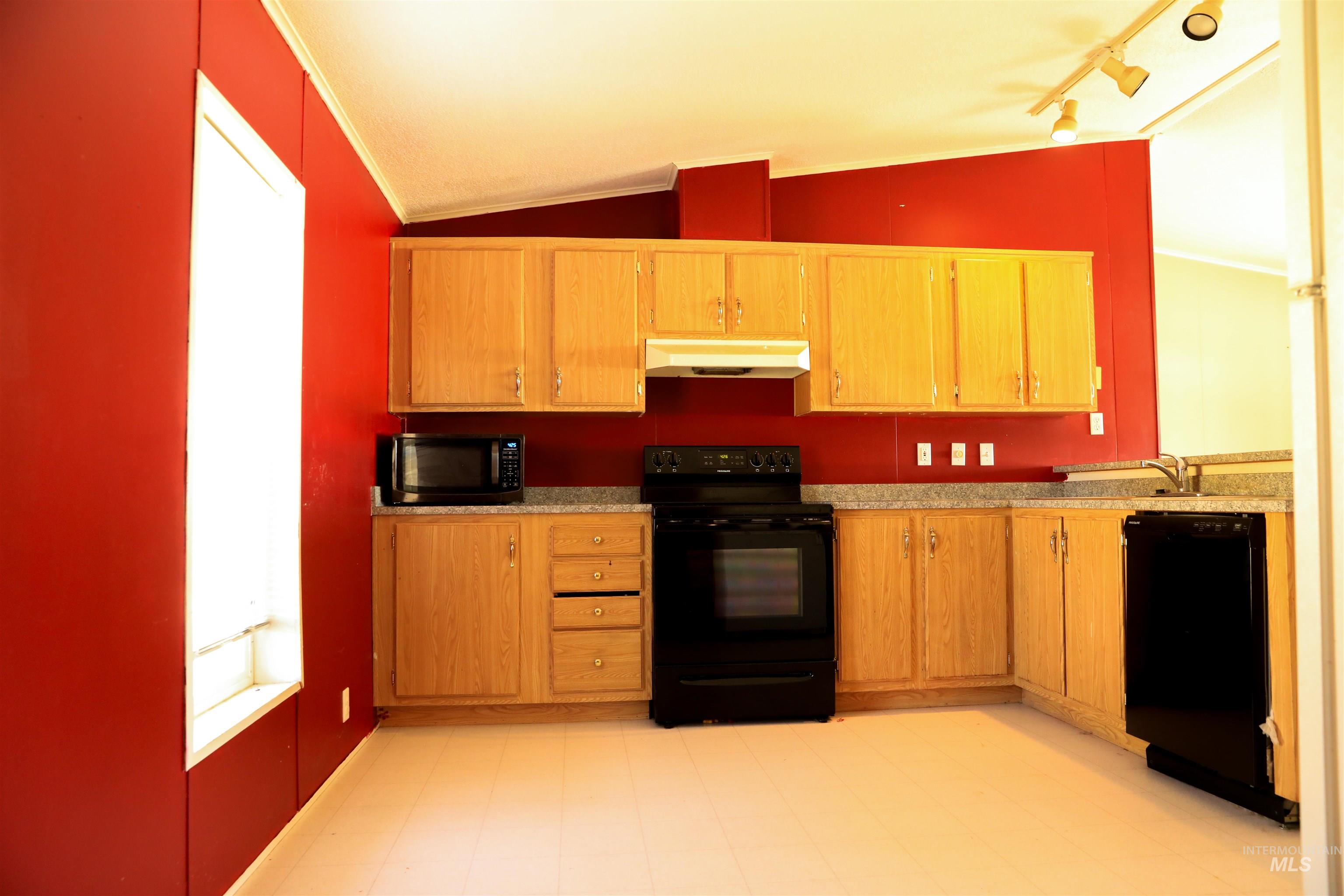 Kitchen featuring black appliances, vaulted ceiling, light countertops, under cabinet range hood, and light flooring